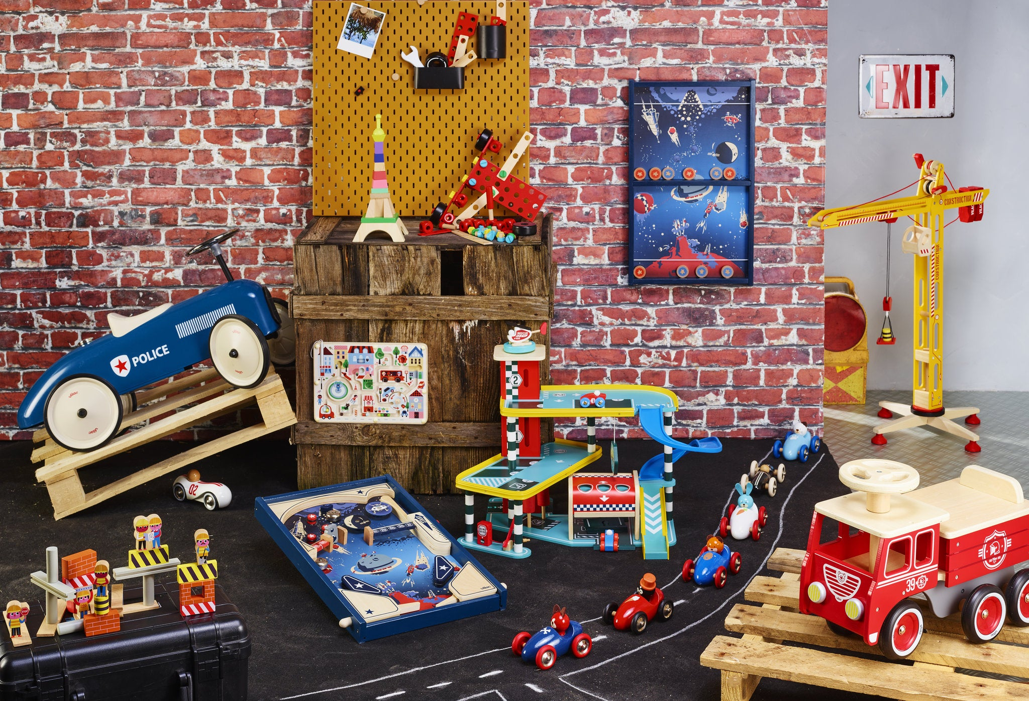 Spielzeugraum mit roter Ziegelwand, Holzautorennbahn, Spielzeugfahrzeugen und einer Parkgarage vor Holzpaletten.