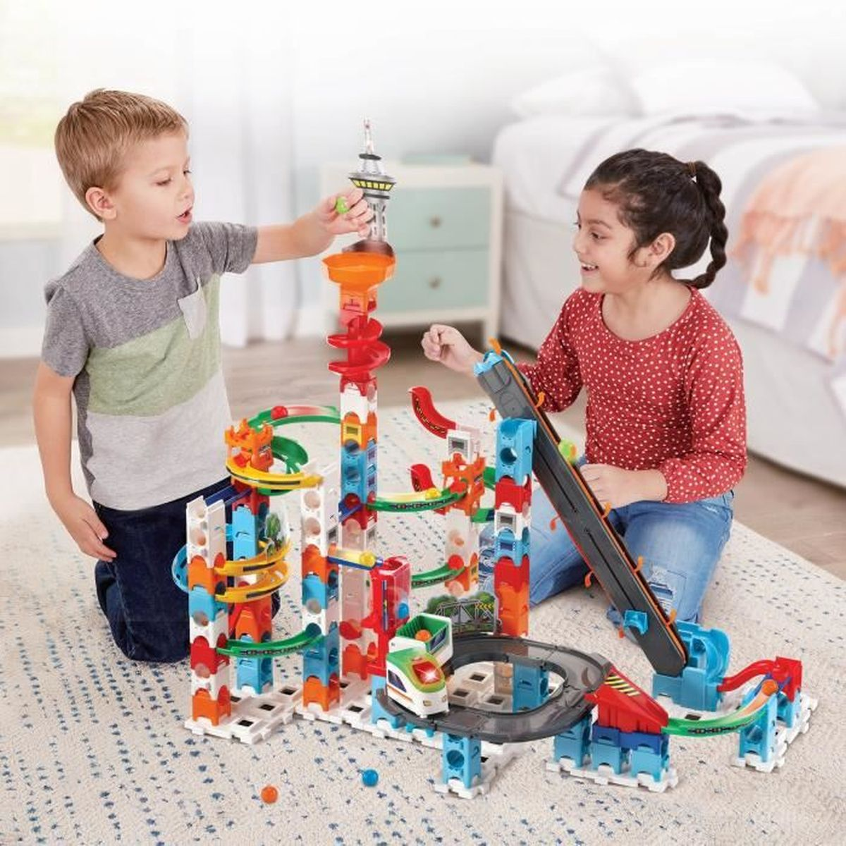 Zwei Kinder spielen auf einem Teppich mit einer bunten Murmelbahn.
