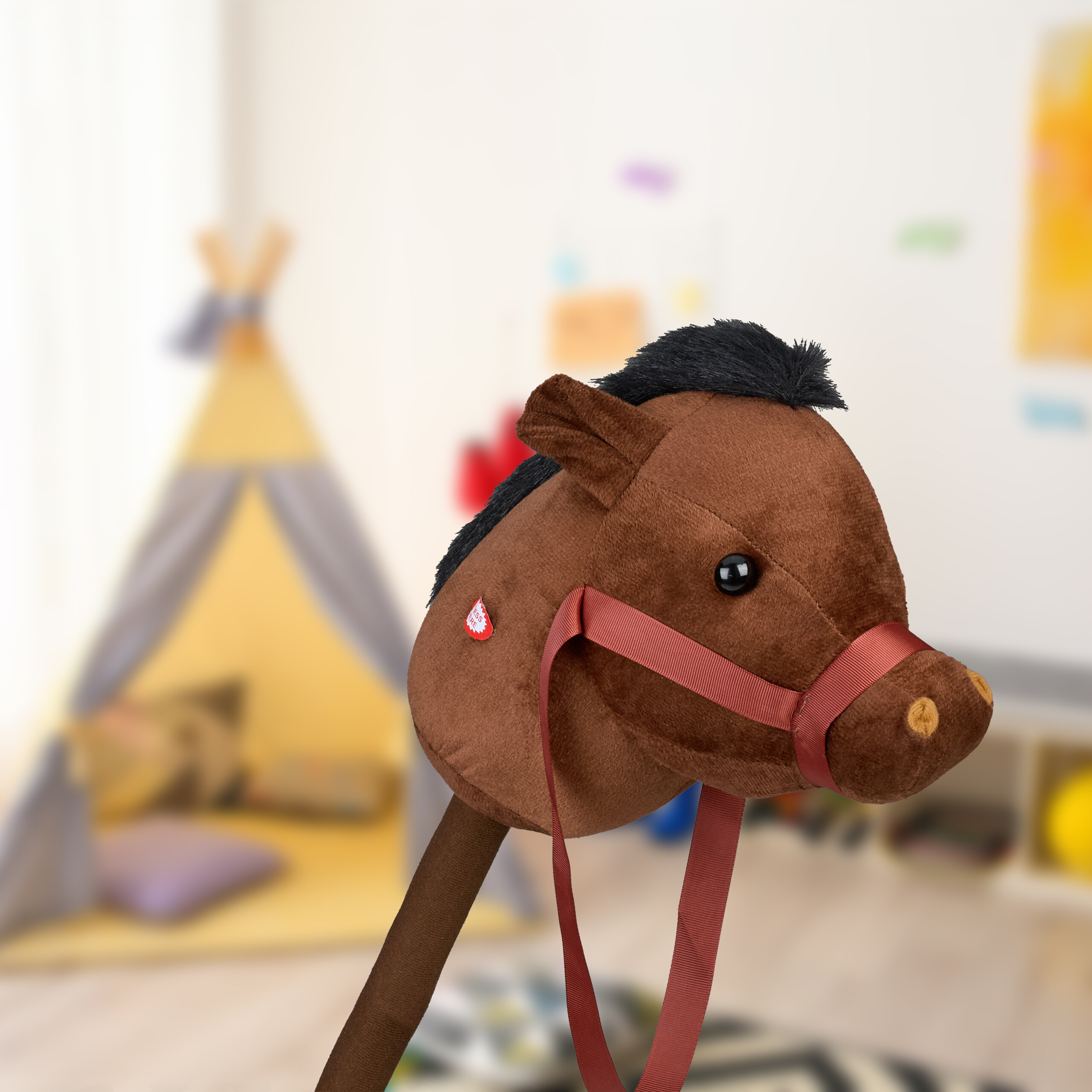 Ein brauner Plüsch-Steckenpferdkopf mit schwarzer Mähne und roten Zügeln in einem Kinderzimmer.