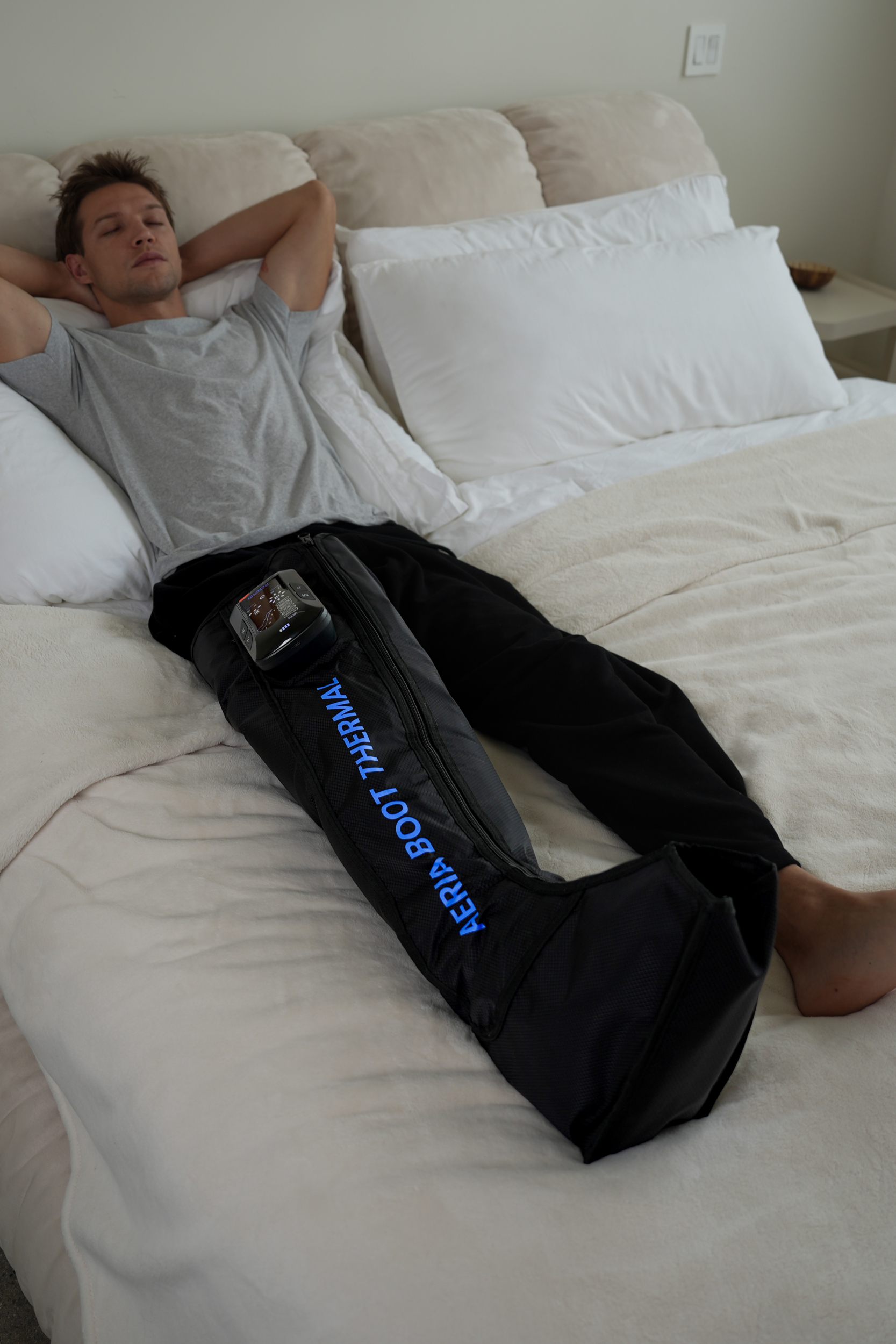 Ein Mann liegt auf dem Bett und trägt eine Aeria Boot Thermal-Beinmanschette.