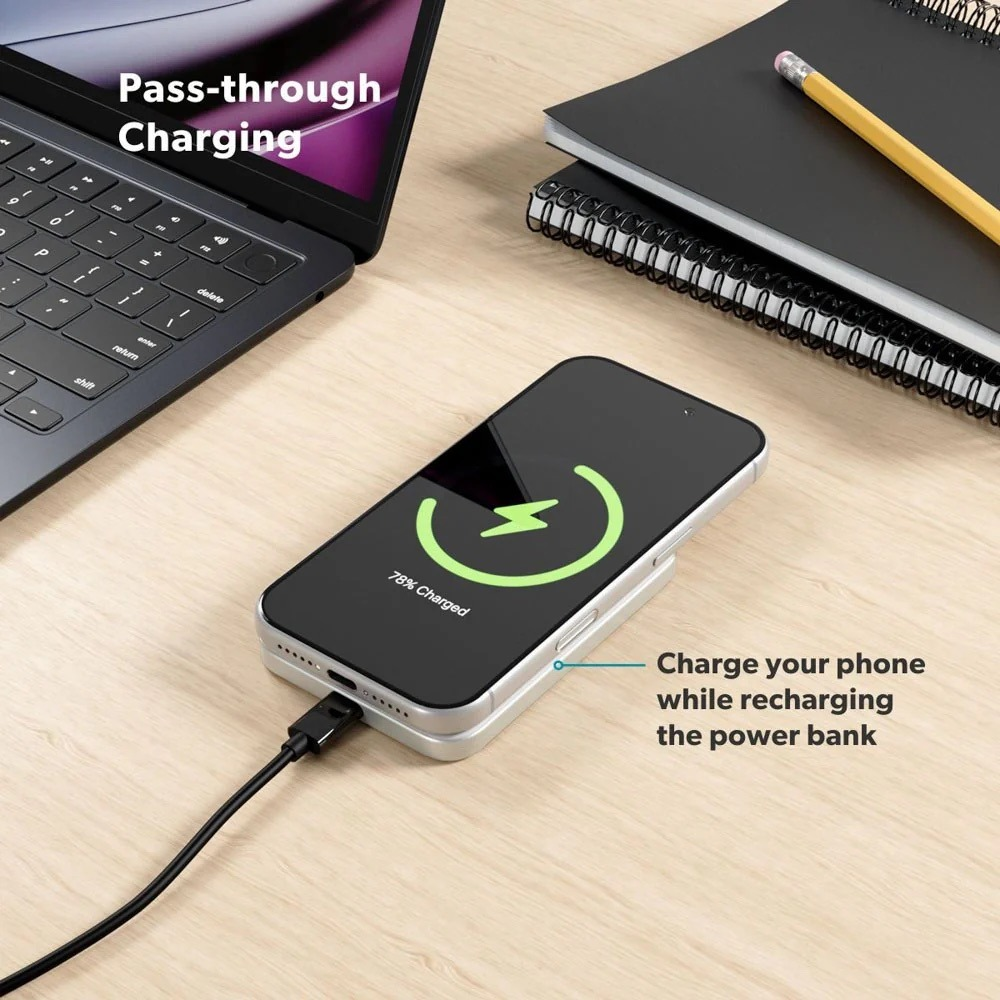 Ein Smartphone lädt auf einer Powerbank auf einem Holzschreibtisch, neben einem Laptop und einem Notizbuch.