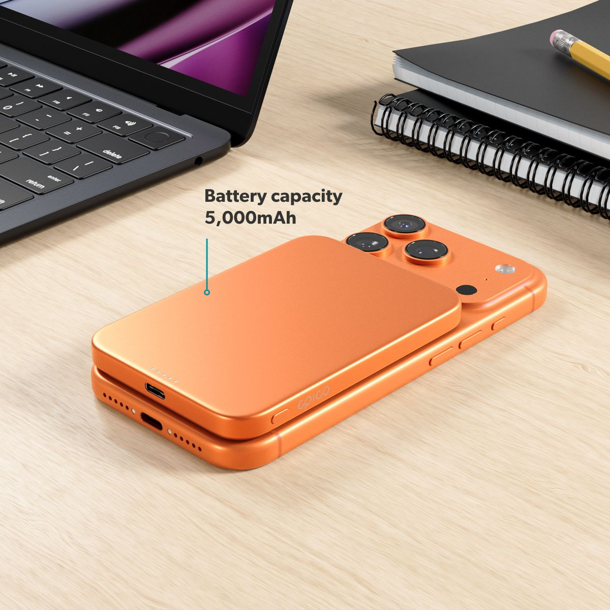 Orangeres Smartphone mit MagSafe-Akku auf Holztisch, neben Laptop und Notizbuch.