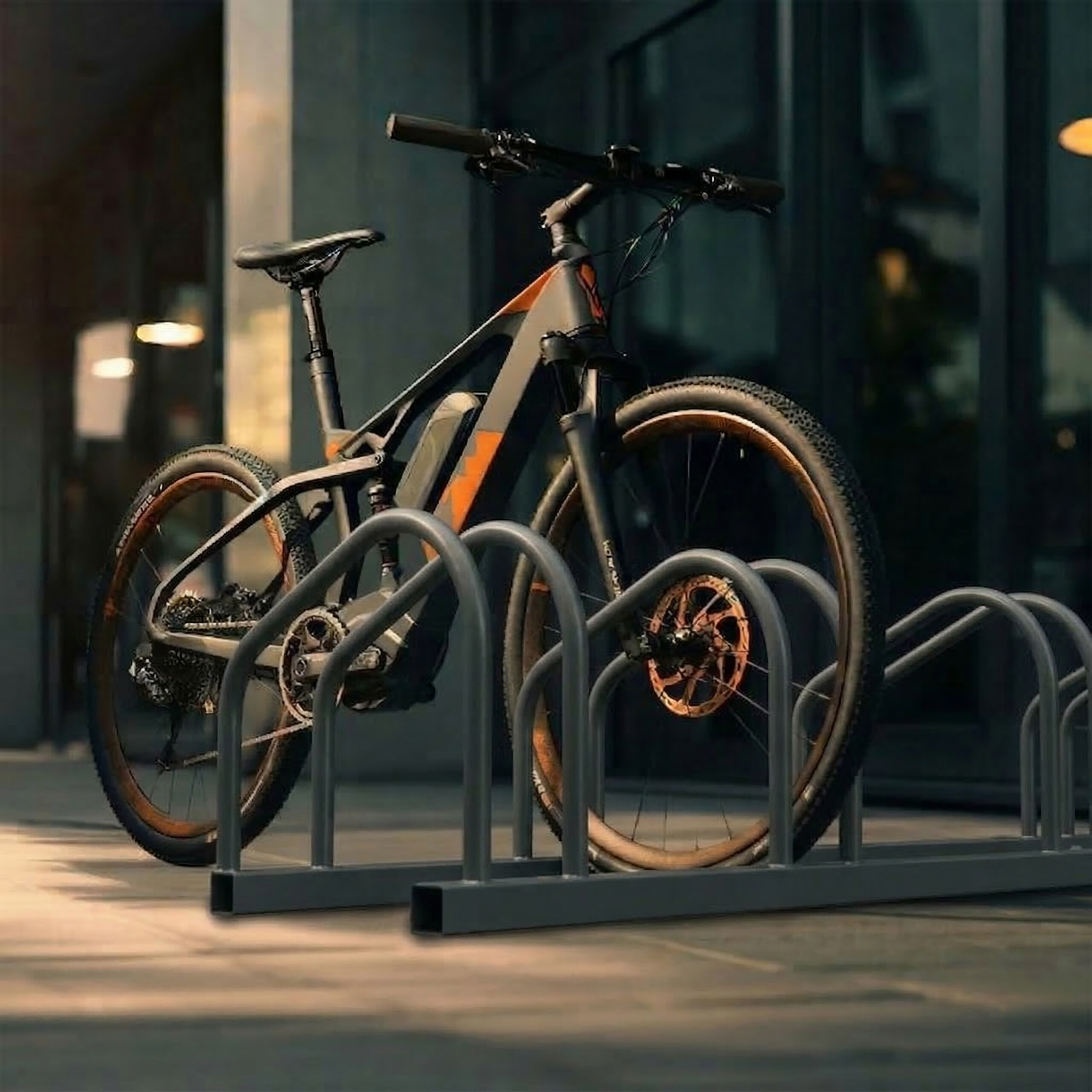 Ein graues E-Bike mit orangen Akzenten parkt in einem grauen Fahrradständer vor einem Gebäude mit Glasfassade.