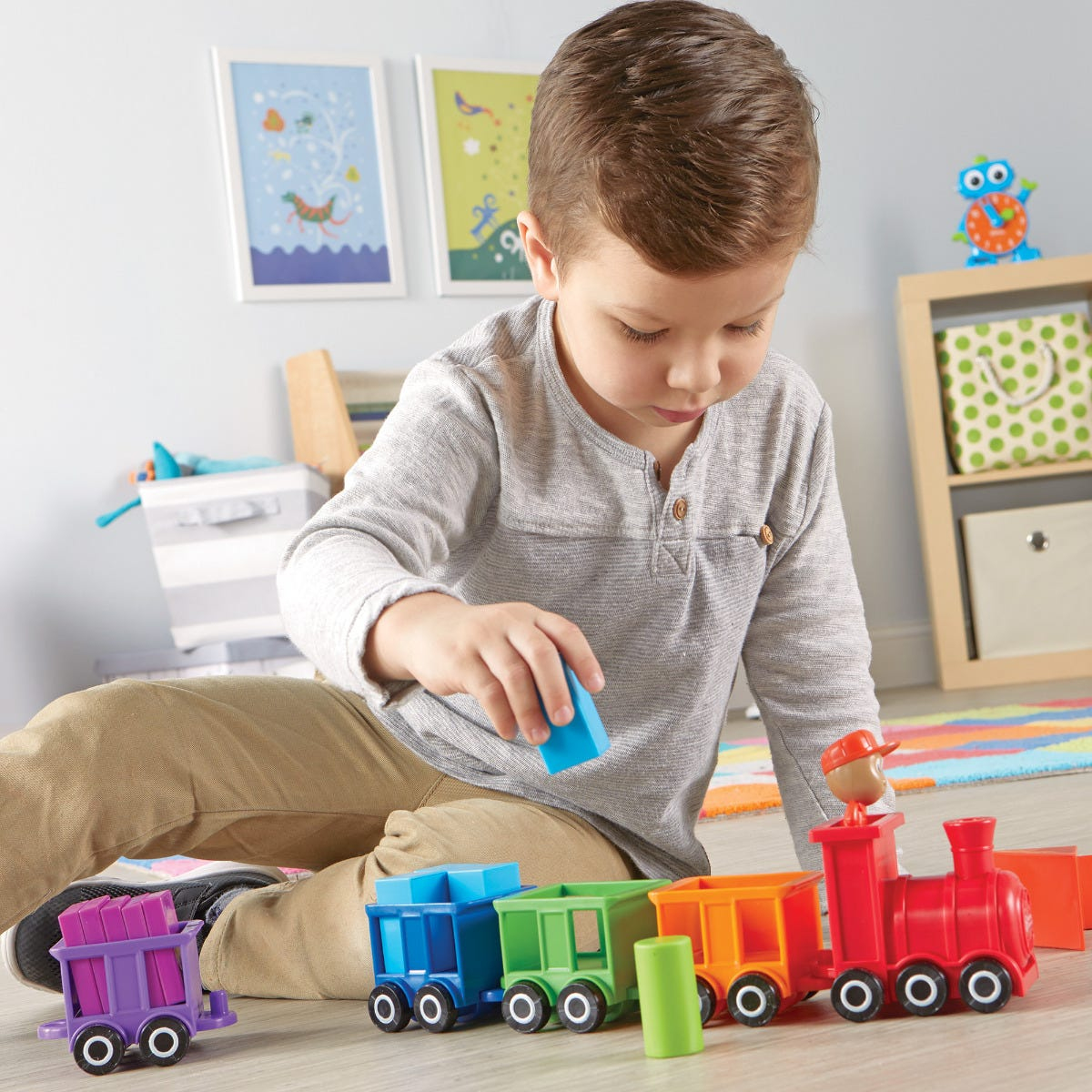 Kleiner Junge sitzt auf dem Boden und spielt mit einem bunten Spielzeugeisenbahn auf Holzfußboden.