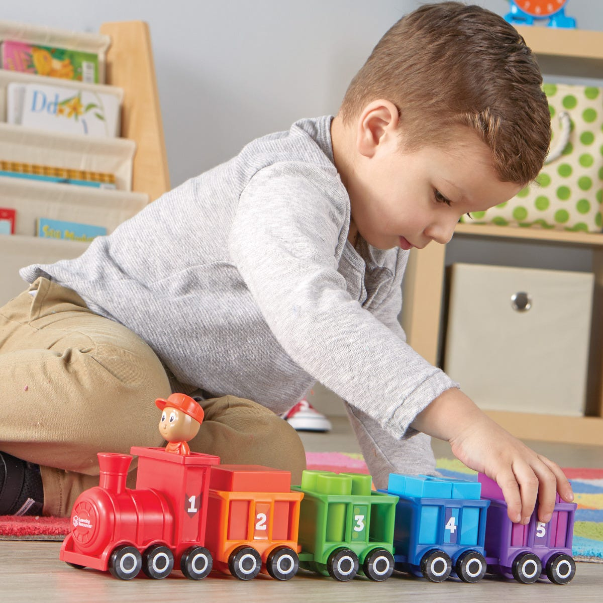 Ein kleiner Junge spielt auf dem Boden eines hellen Raumes mit einem bunten Zahleneisenbahn-Spielzeug.