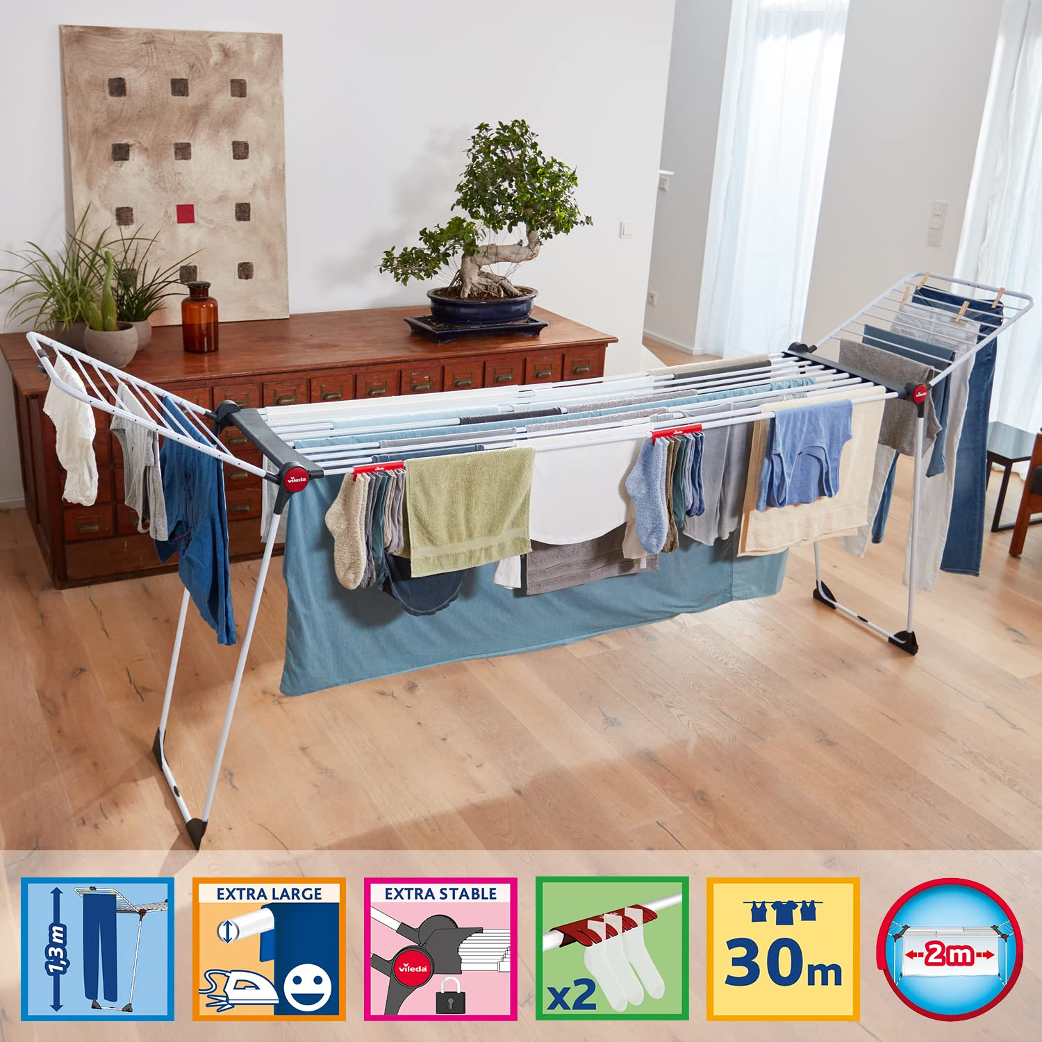 Ein weißer Wäscheständer voller Kleidung und Handtücher steht in einem modernen Wohnzimmer mit Holzboden.