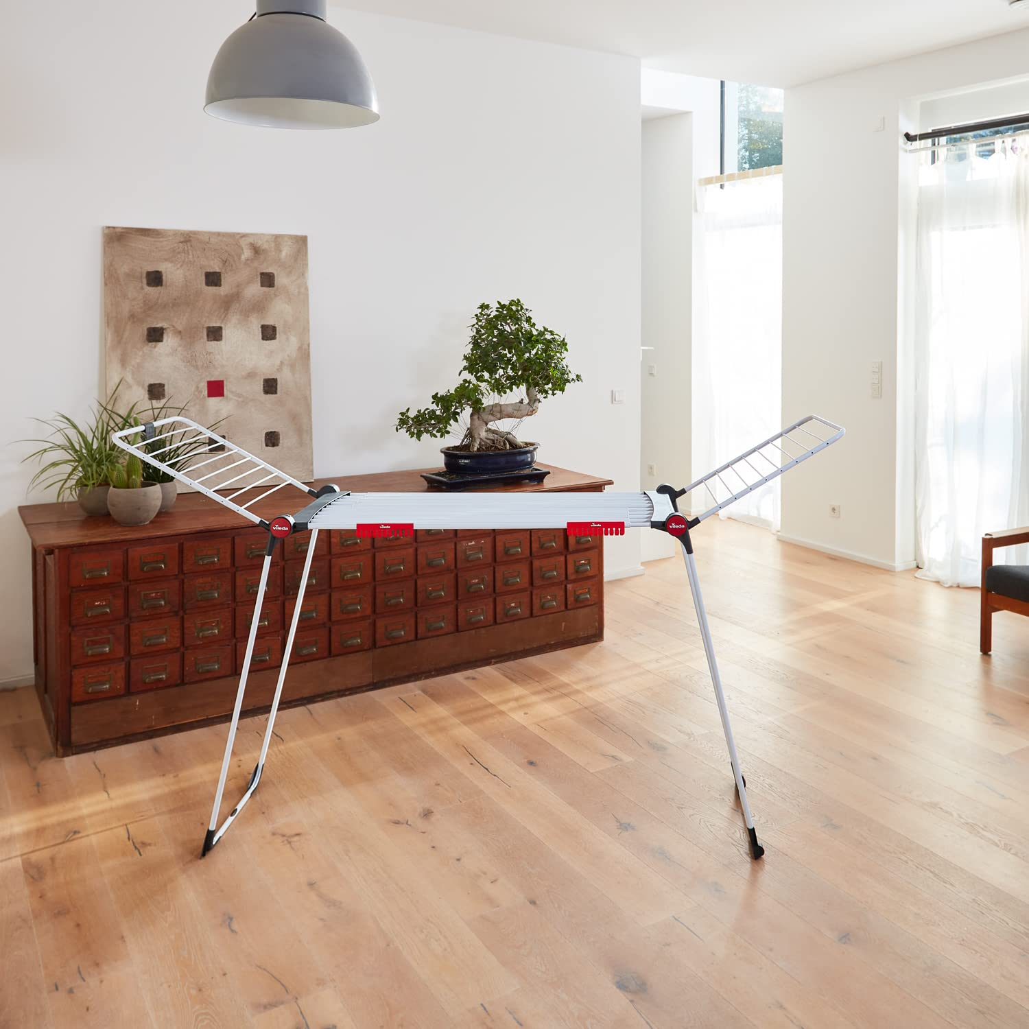 Ein Wäscheständer steht in einem hellen Wohnzimmer mit Holzmöbeln und einem Bonsai.