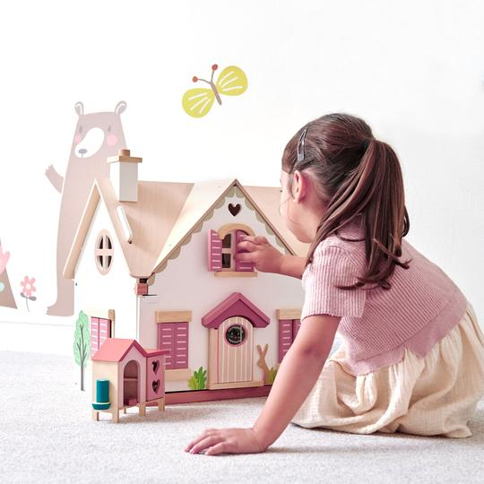 Ein kleines Mädchen spielt im Kinderzimmer mit einem bunten Holzpuppenhaus vor einer gemalten Bärentapete.