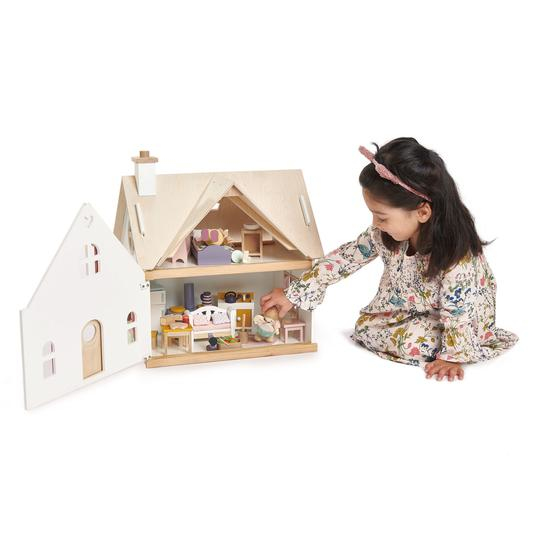 Ein kleines Mädchen spielt mit einem Puppenhaus aus Holz auf weißem Boden.