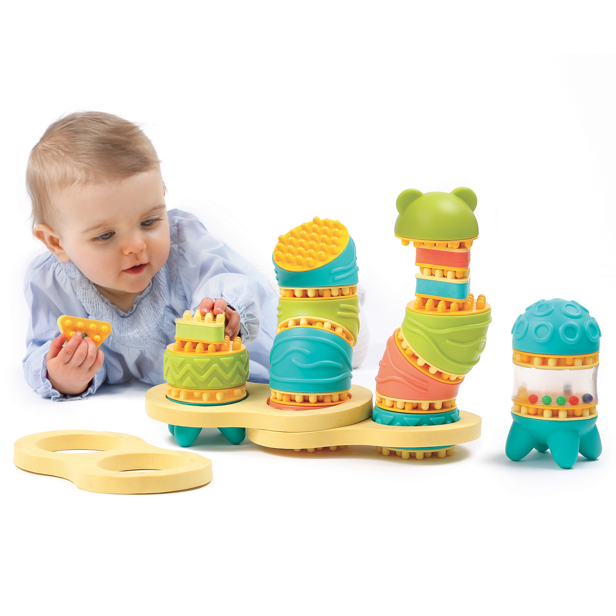 Baby in blauem Hemd spielt auf weißem Boden mit bunten Steckspielzeug-Türmen.