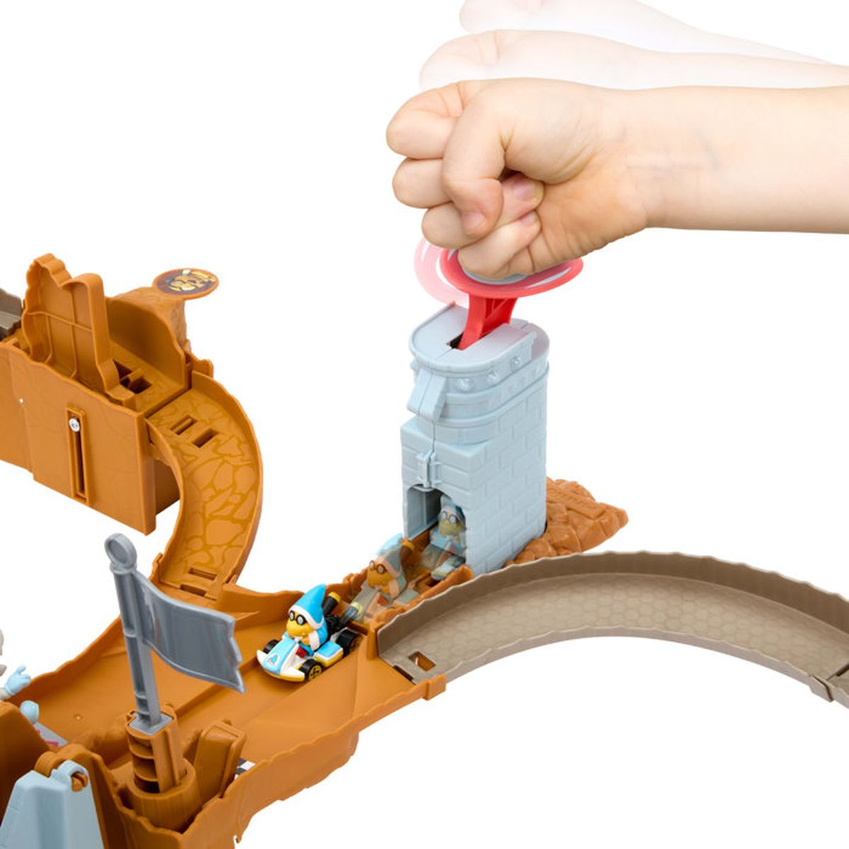 Eine Hand drückt auf den roten Auslöser eines blauen Turms, während Spielzeugautos auf einer Rennstrecke fahren.