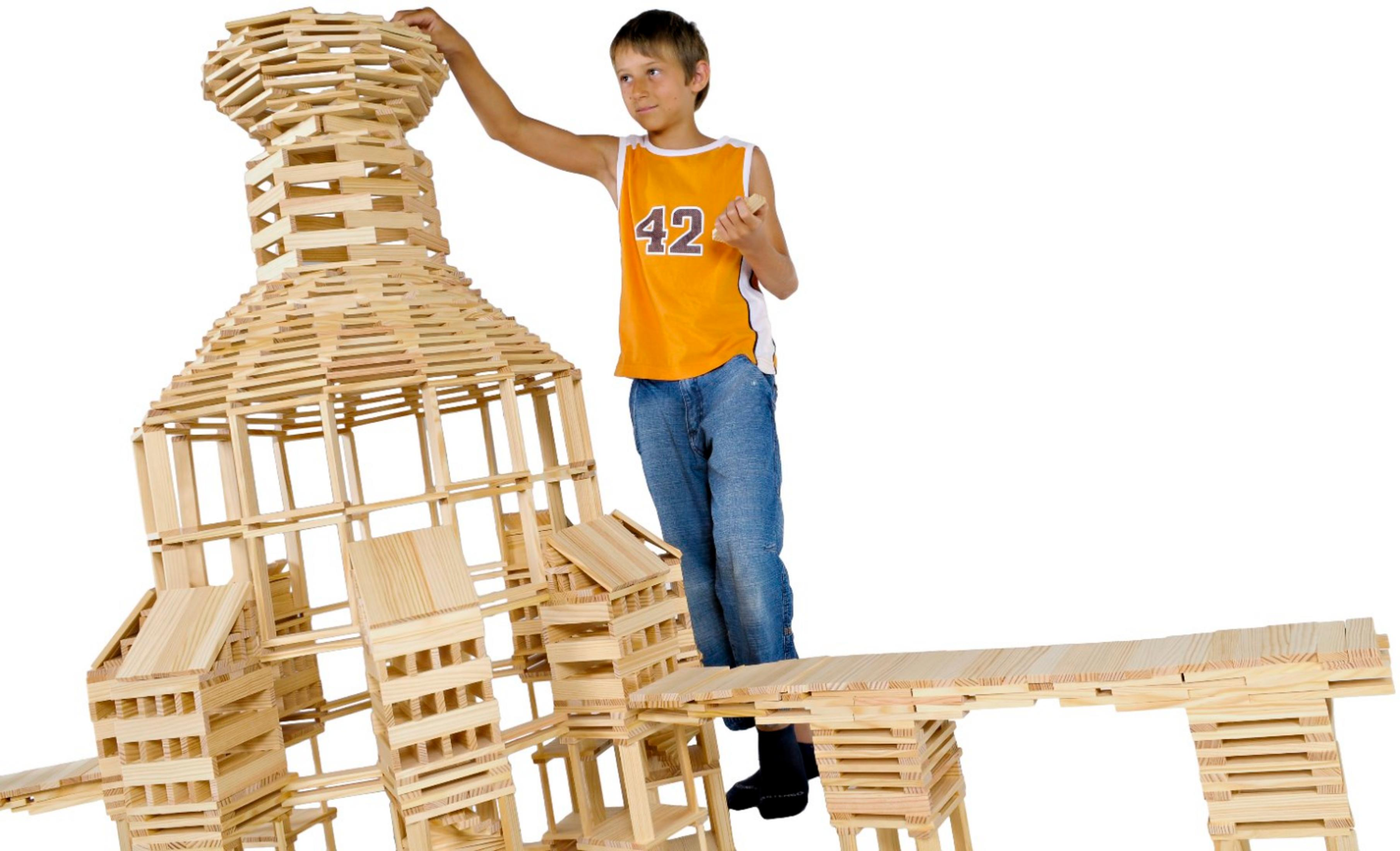 Ein Junge in einem orangefarbenen Trikot baut eine große Struktur aus Holzklötzen gegen einen weißen Hintergrund.