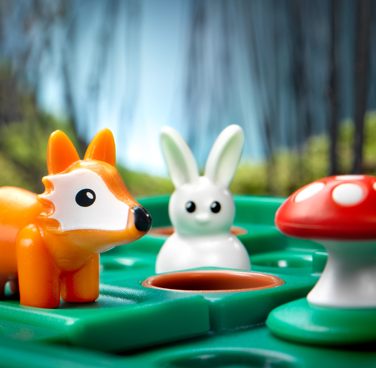 Spielzeug-Fuchs und Hase aus Kunststoff stehen auf einem grünen Brett neben einem roten Pilz vor verschwommenem Hintergrund.