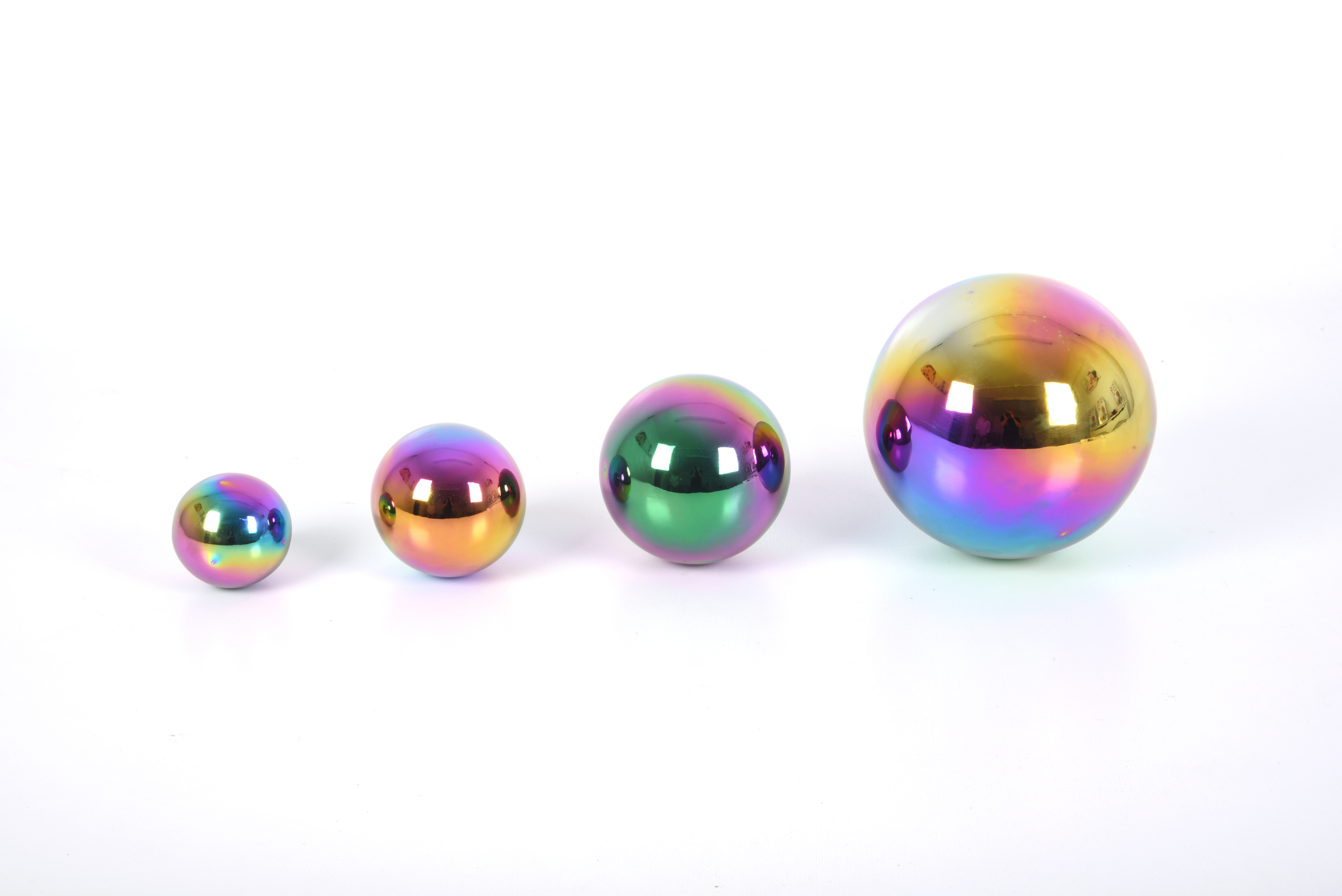 Vier glänzende, regenbogenfarbene Kugeln in verschiedenen Größen stehen in einer Reihe vor weißem Hintergrund.