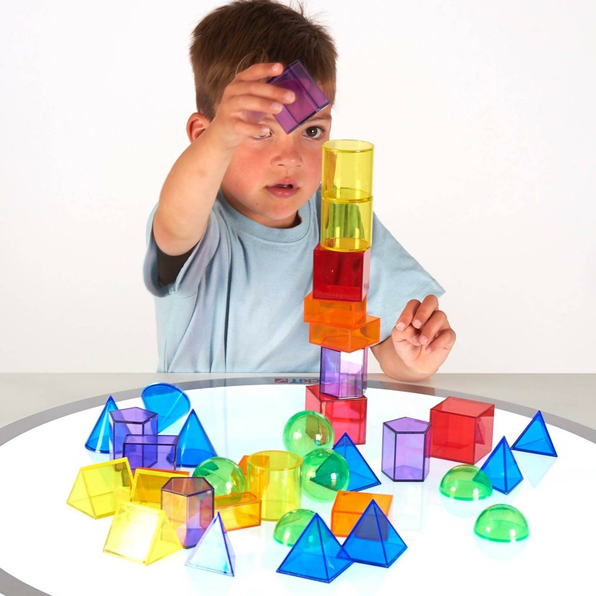 Ein Junge stapelt bunte, transparente geometrische Formen auf einer leuchtenden Platte.