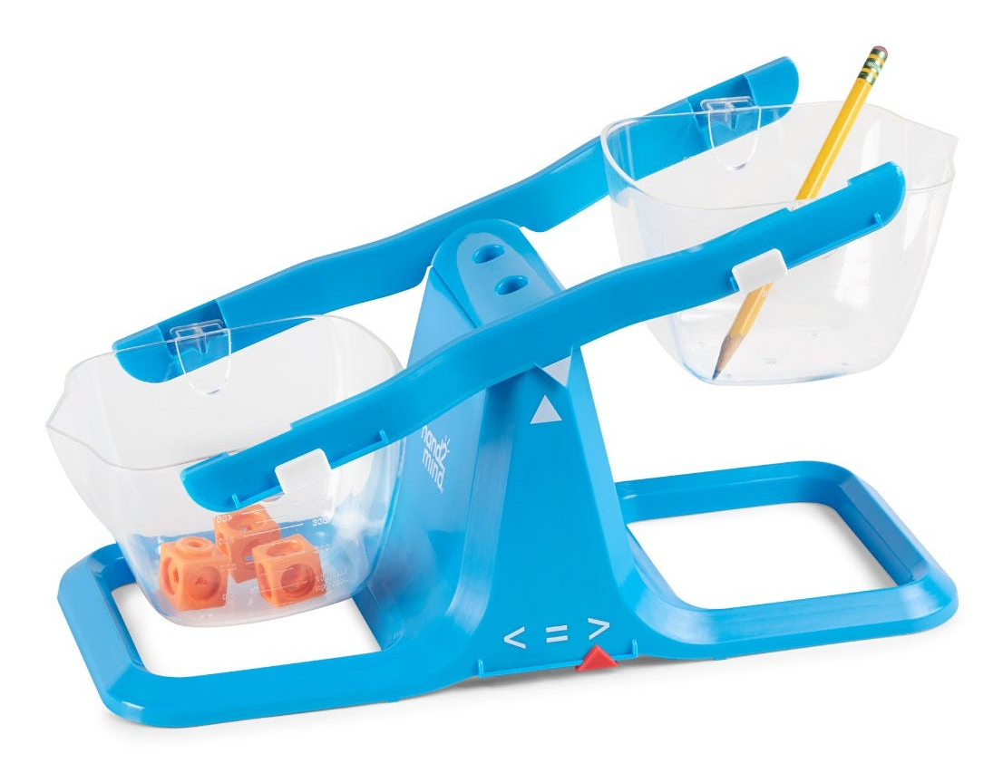 Eine blaue Kunststoffwaage mit zwei durchsichtigen Eimern hält orangefarbene Würfel und einen gelben Bleistift.