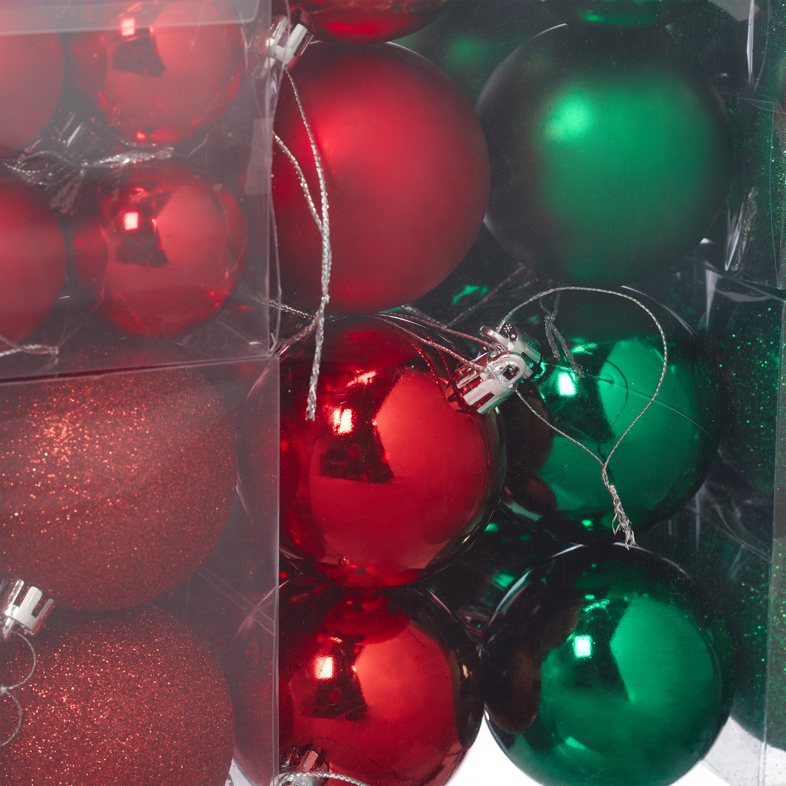 Rote und grüne Weihnachtskugeln in transparenten Kunststoffschachteln.