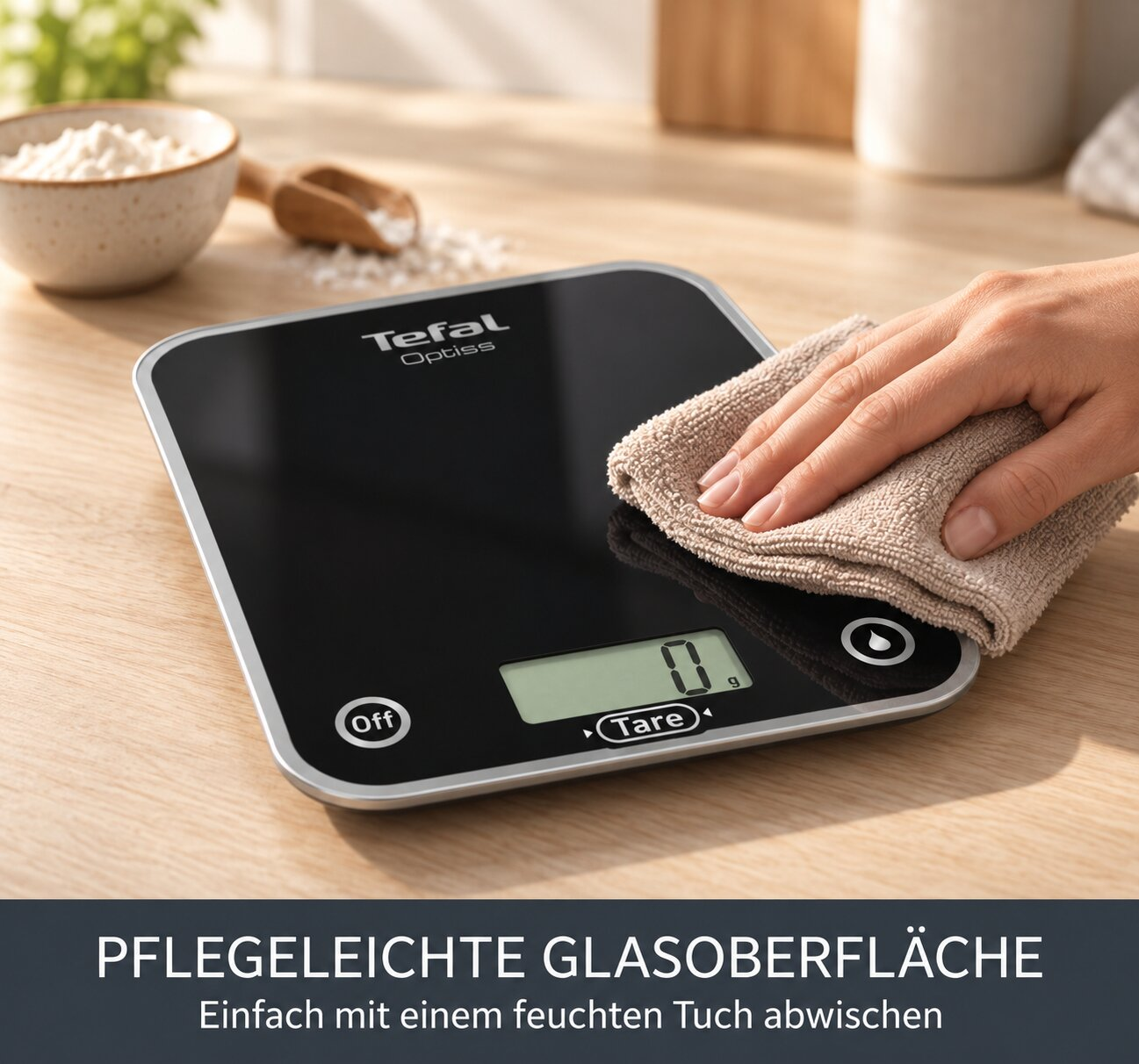 Eine Hand wischt eine schwarze Tefal Küchenwaage mit einem feuchten Tuch ab.