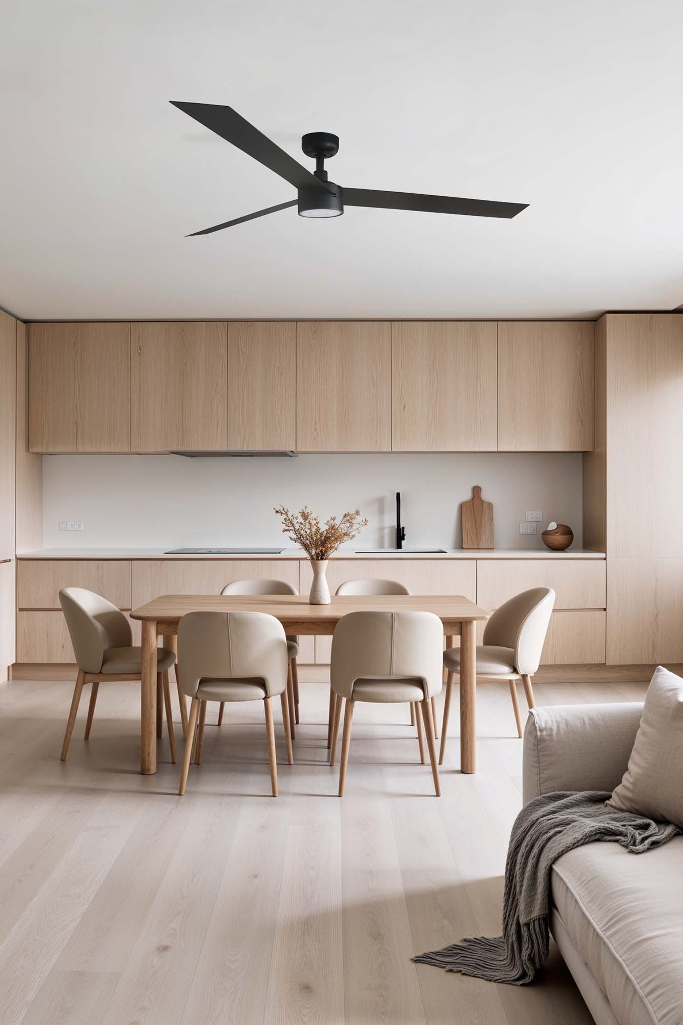 Moderne Küche mit Holzschränken, Esstisch mit hellen Stühlen, schwarzem Deckenventilator und hellen Holzböden.