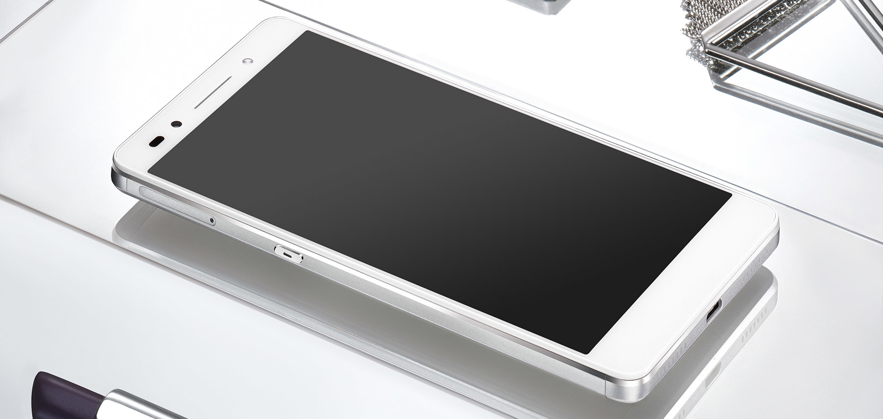 Ein weißes Smartphone liegt auf einer glänzenden weißen Oberfläche neben einem Drahtobjekt.