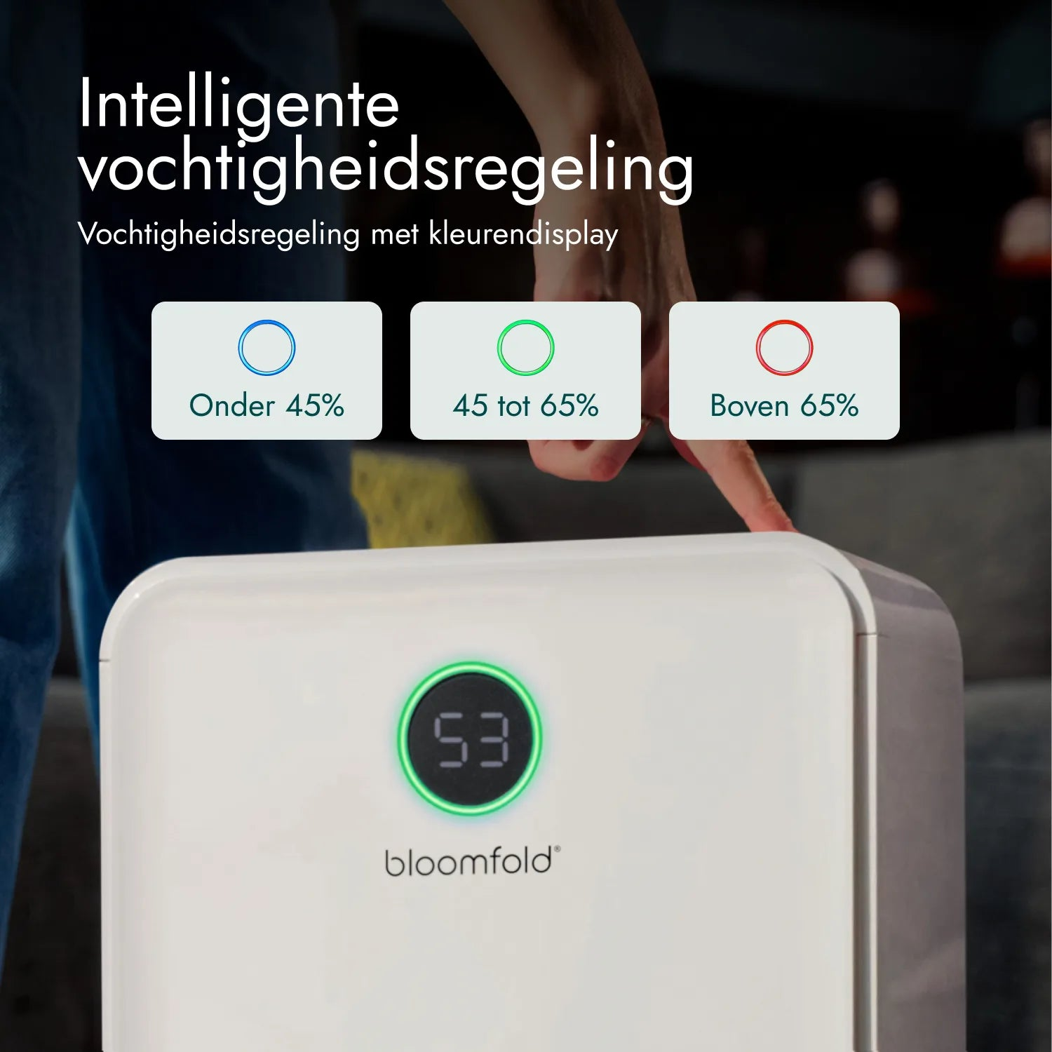 Eine Person zeigt auf einen weißen Bloomfold Luftentfeuchter mit Feuchtigkeitsindikatoren in Blau, Grün und Rot.