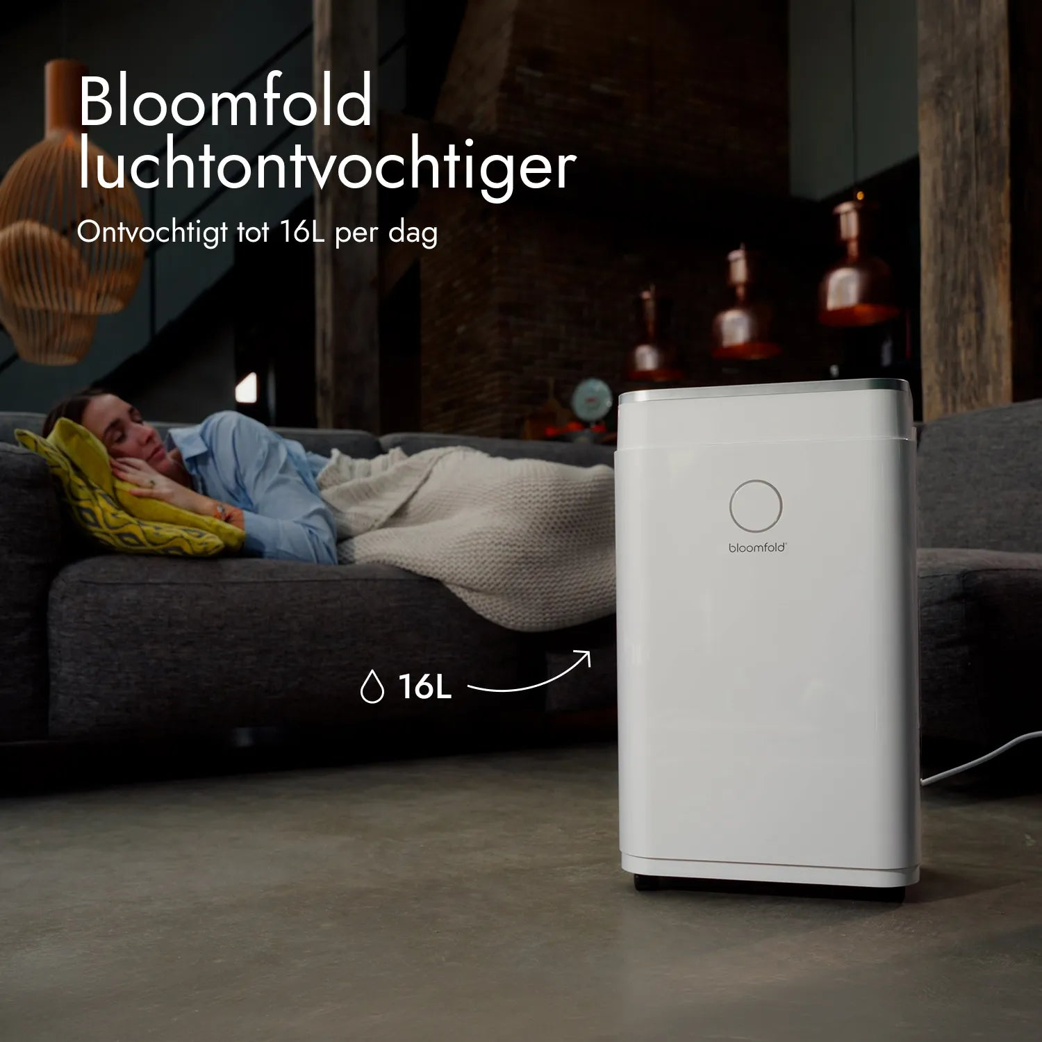 Ein weißer Bloomfold Luftentfeuchter steht auf dem Boden, während eine Frau im Hintergrund auf einem Sofa schläft.