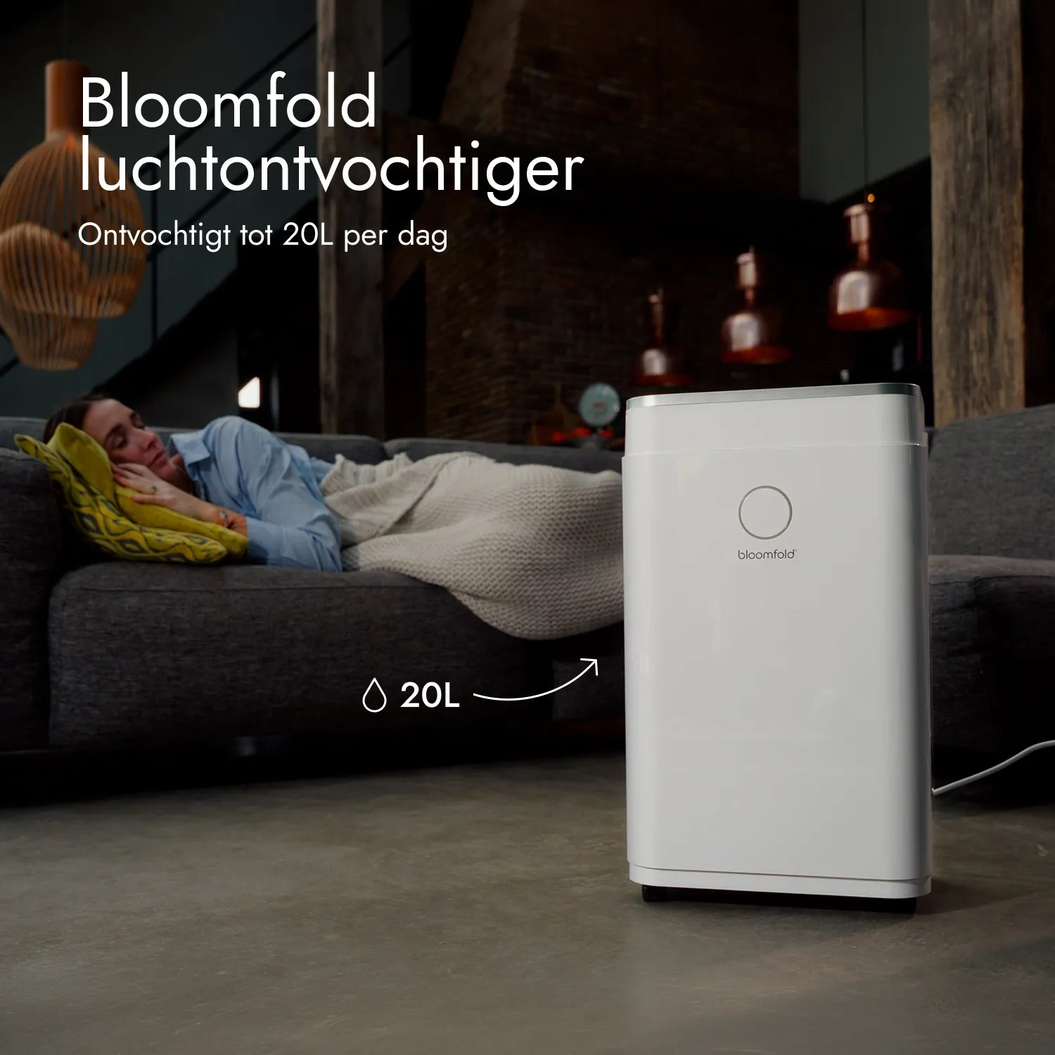 Ein weißer Luftentfeuchter steht auf dem Boden, während eine Frau im Hintergrund auf einem Sofa schläft.