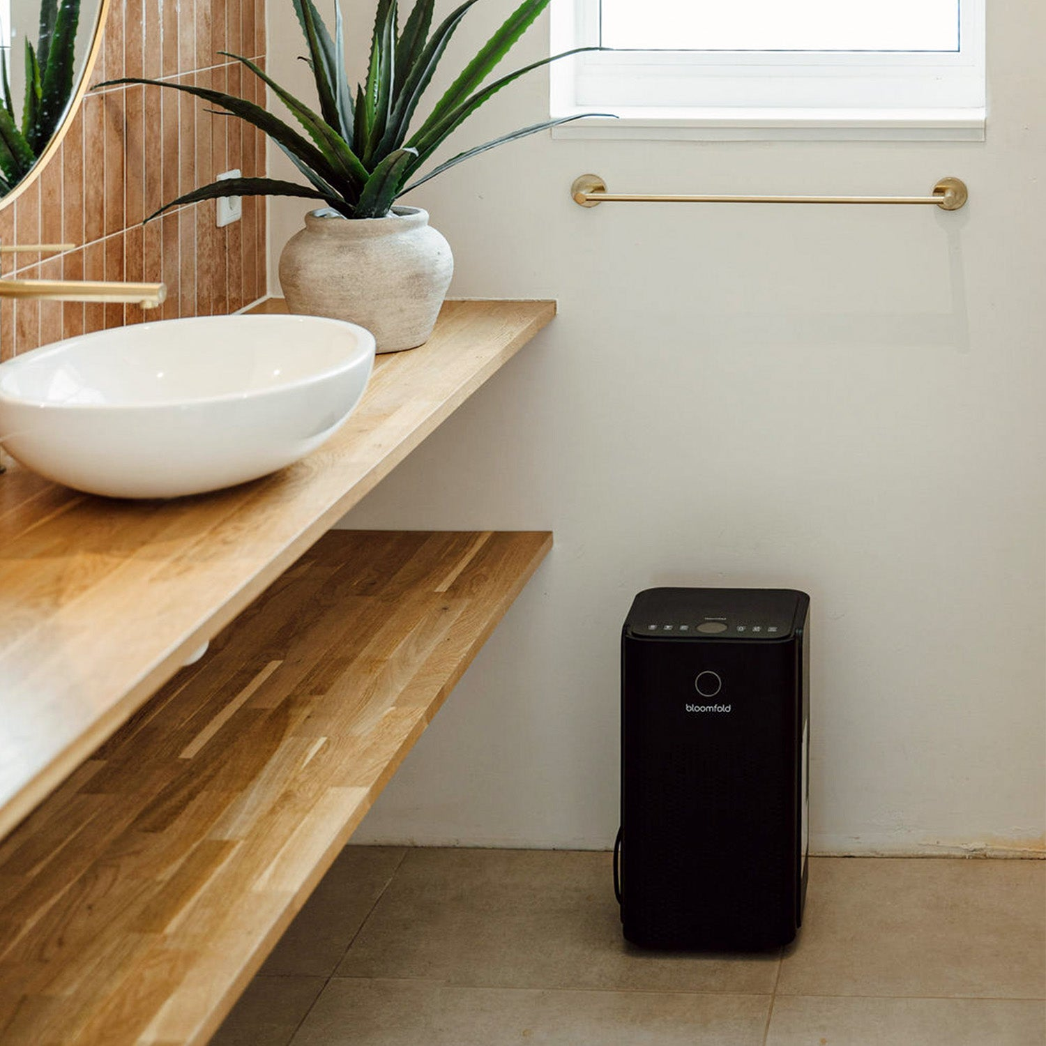 Ein schwarzer Luftentfeuchter steht auf dem Fliesenboden eines hellen Badezimmers neben einem Waschtisch.