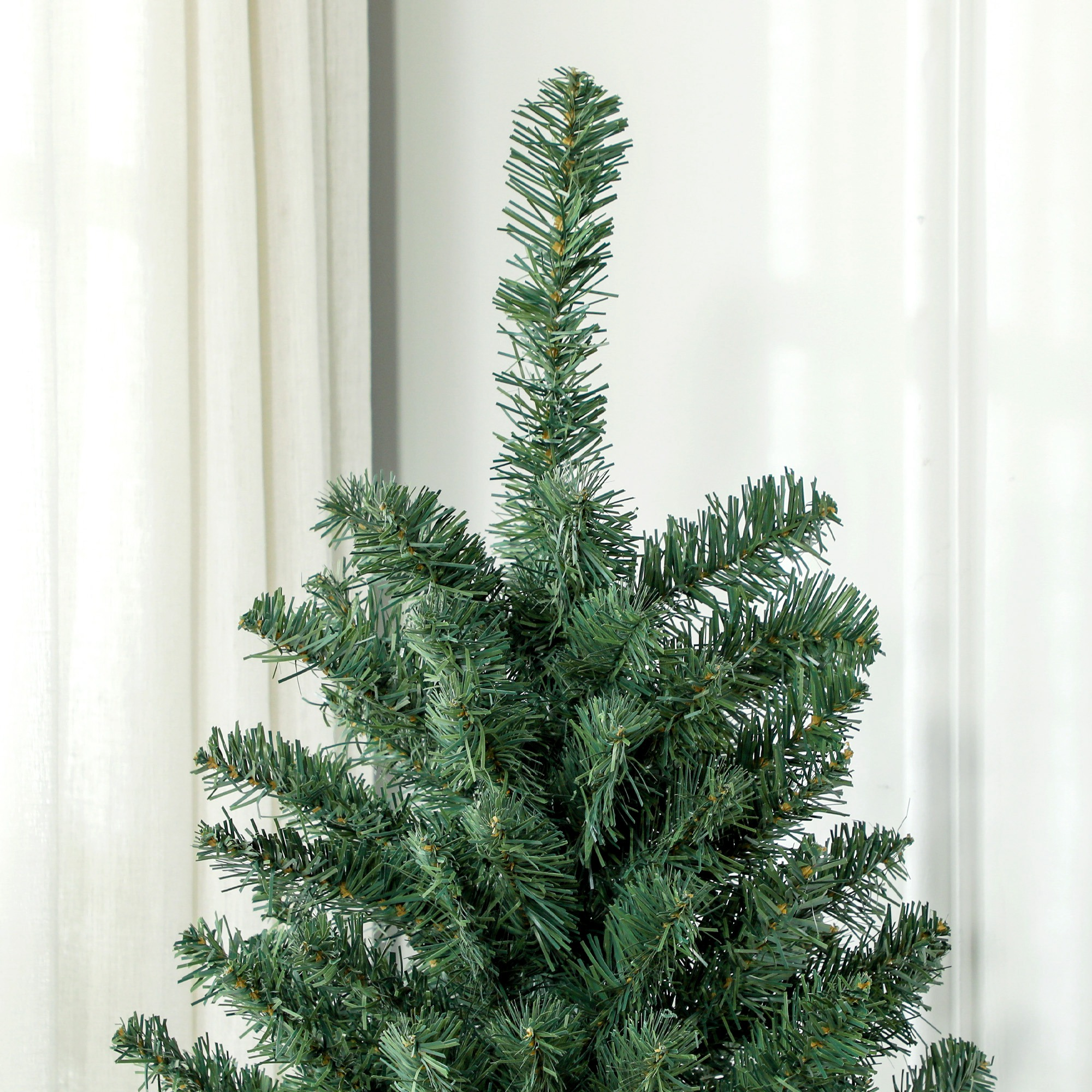 La parte superior de un árbol de Navidad artificial verde frente a una cortina blanca.
