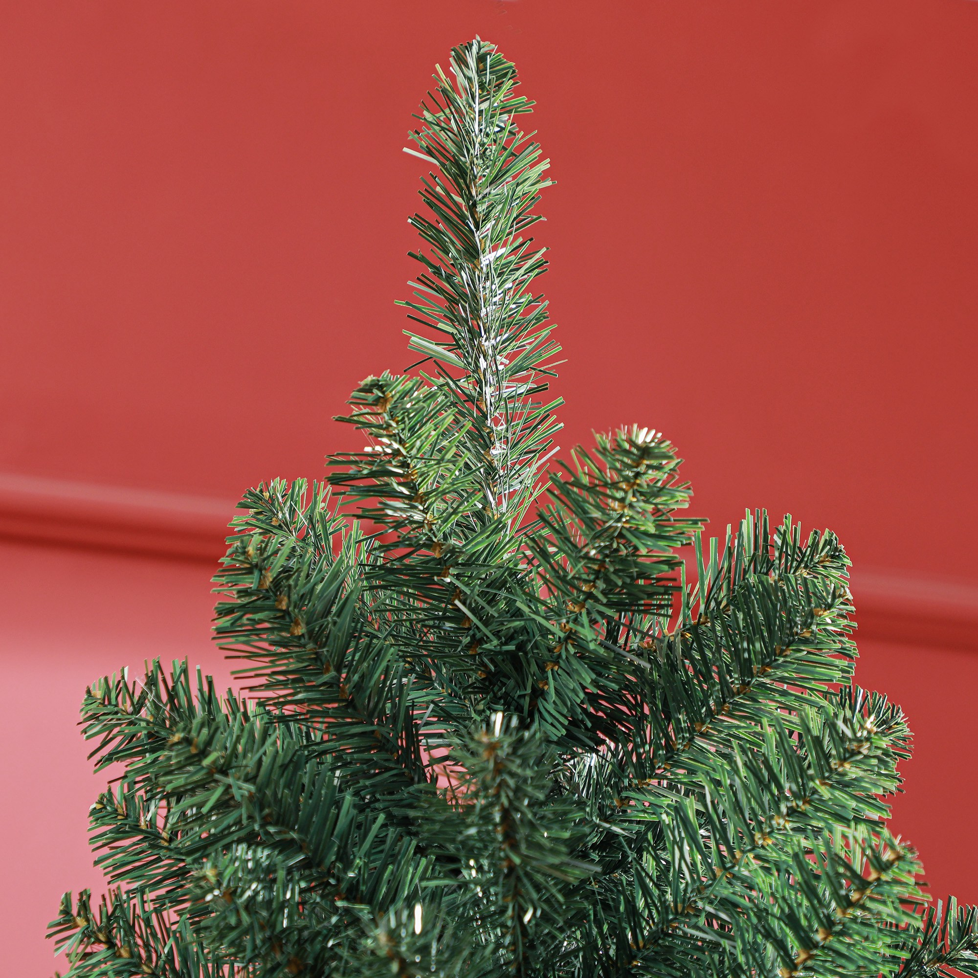 Primer plano de la copa de un árbol de Navidad artificial verde contra una pared roja.