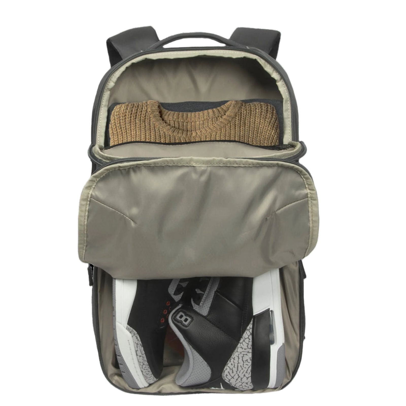 Una mochila gris abierta con un suéter marrón en el compartimento principal y zapatillas abajo.
