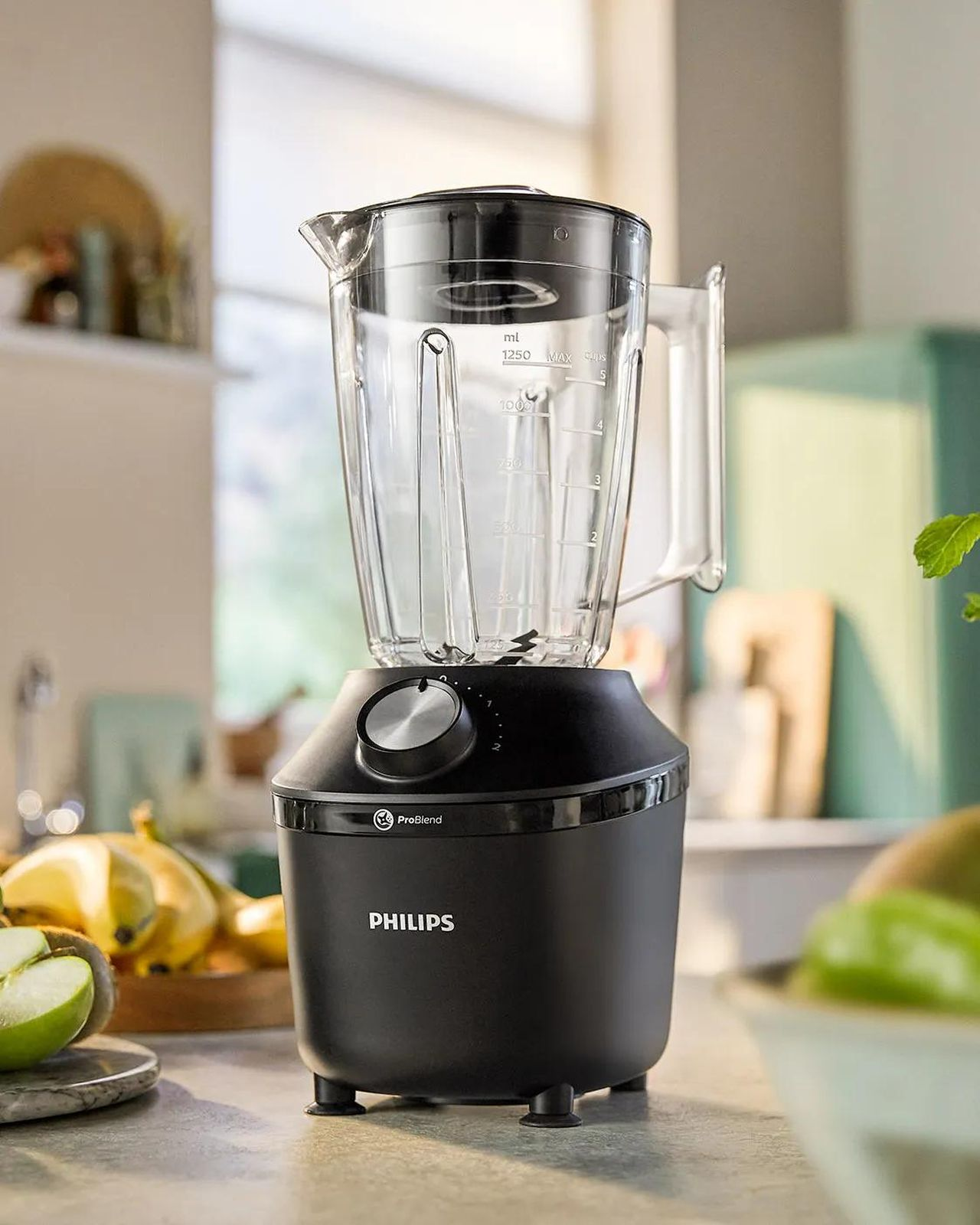 Una licuadora Philips negra sobre una encimera de cocina con fruta de fondo.