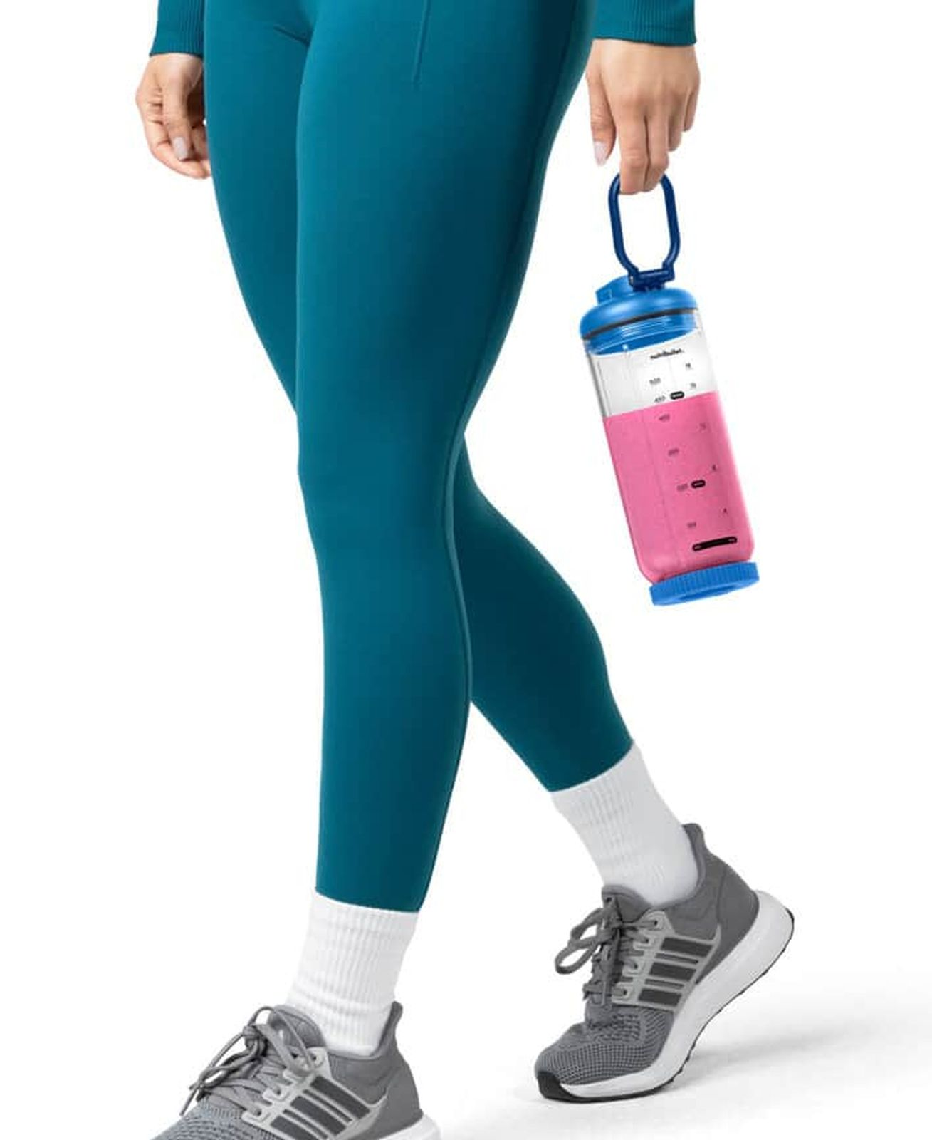 Eine Frau in Leggings hält eine blaue Trinkflasche mit rosa Inhalt und trägt graue Turnschuhe.