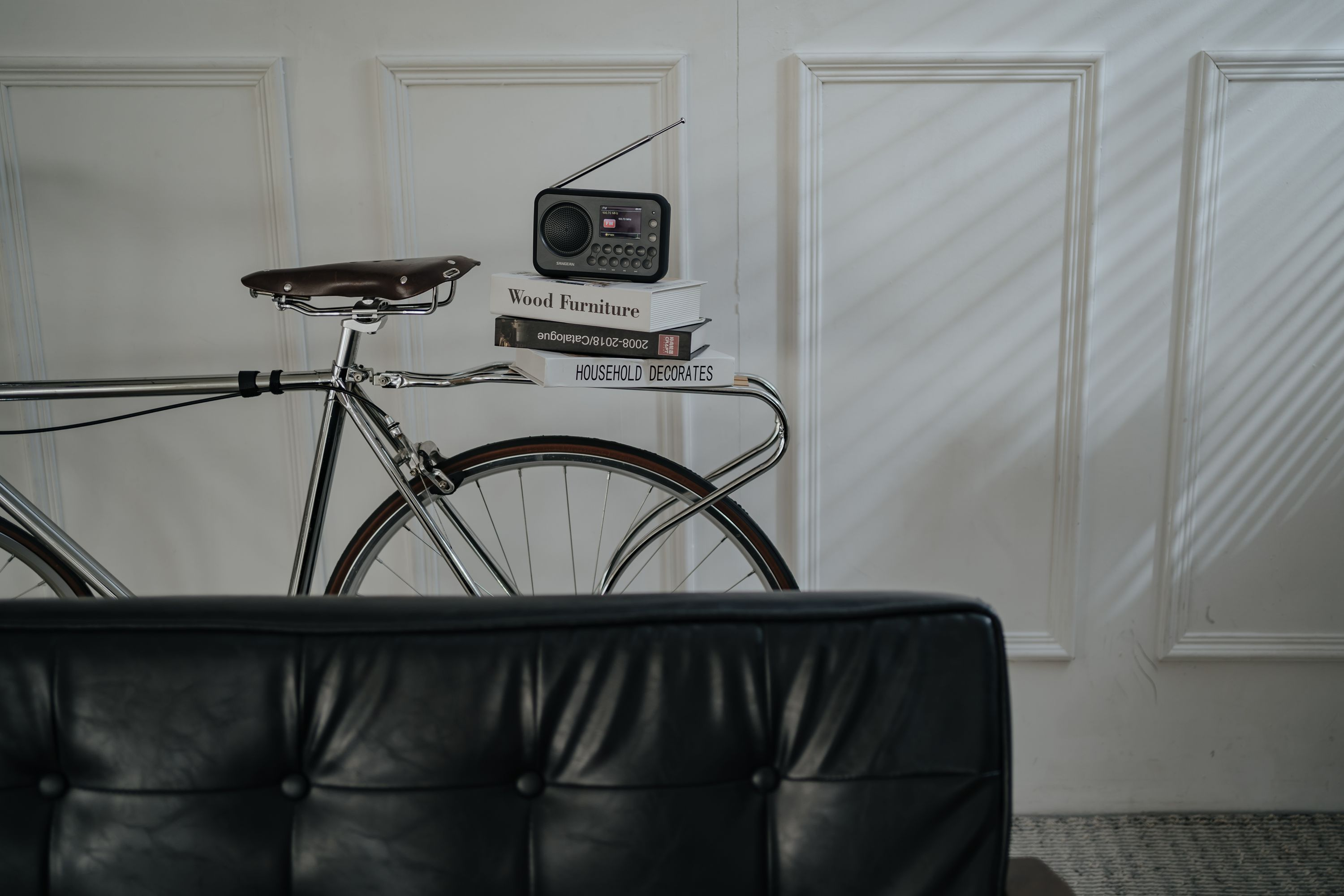 Ein Vintage-Fahrrad mit stapelbaren Büchern und einem Radio auf dem Gepäckträger, hinter einem Ledersofa.