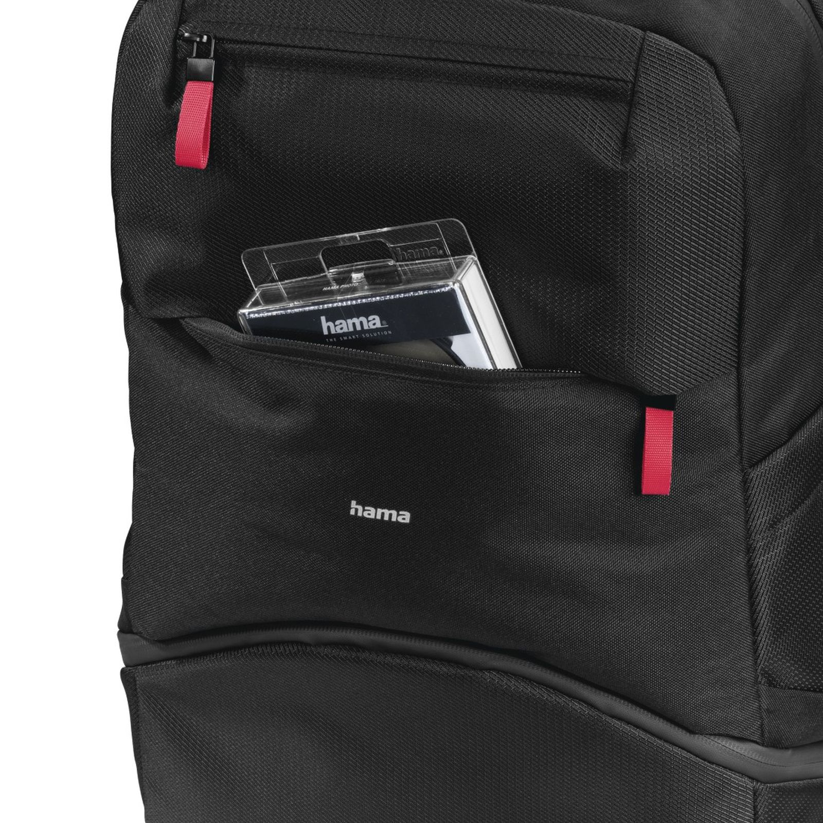 Schwarzer Hama Rucksack mit Vordertasche, in der eine Hama Verpackung steckt und kleine rote Zierbänder.