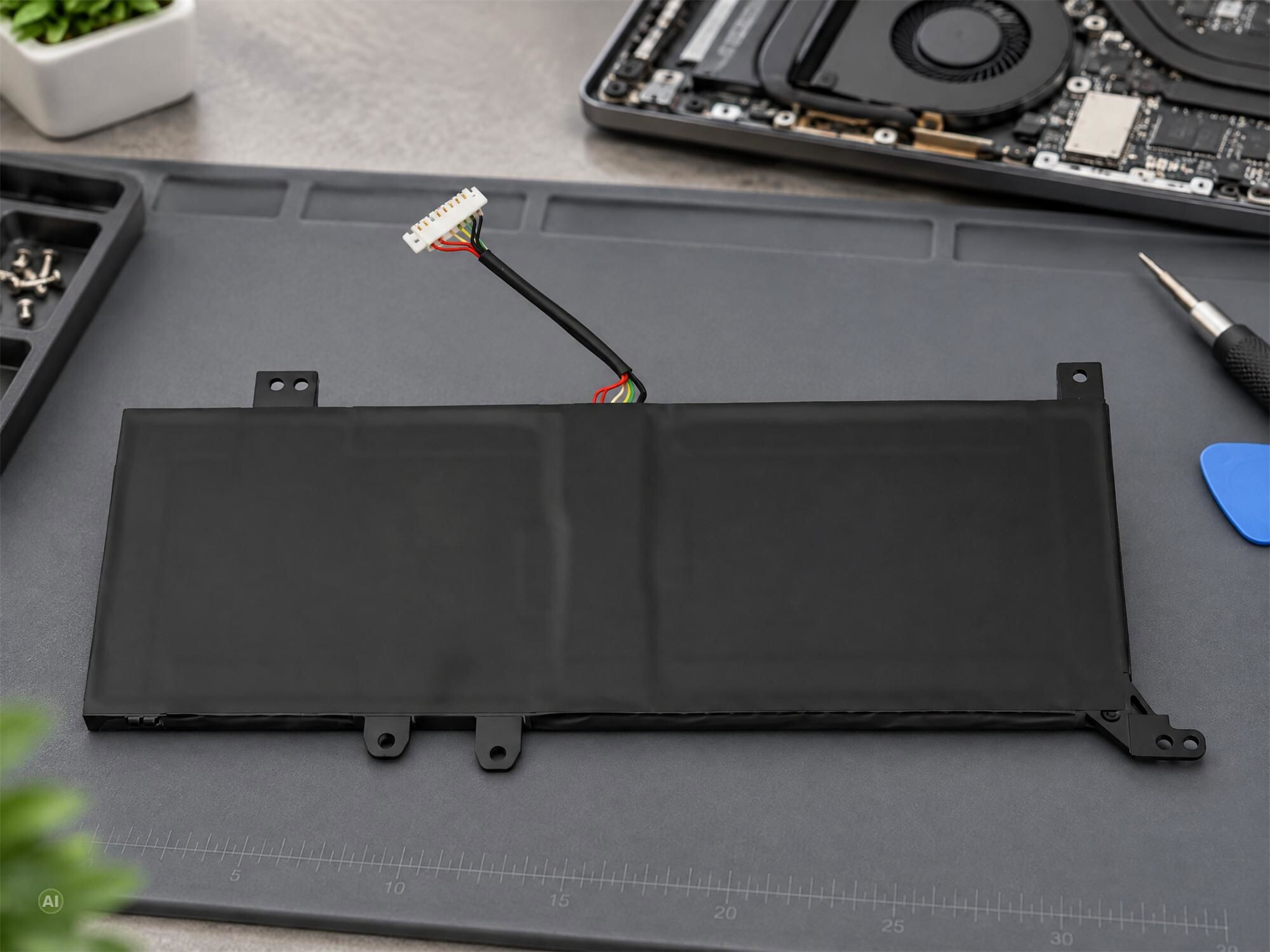 Ein flacher schwarzer Laptop-Akku mit Kabel liegt auf einer grauen Reperaturmatte mit Werkzeugen.