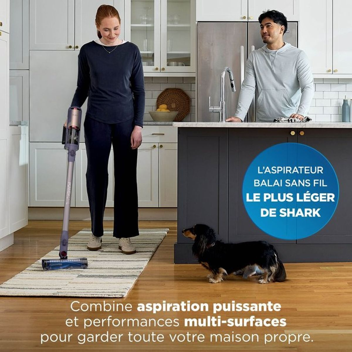 Una donna usa un aspirapolvere senza fili leggero in cucina mentre un uomo e un cane guardano.