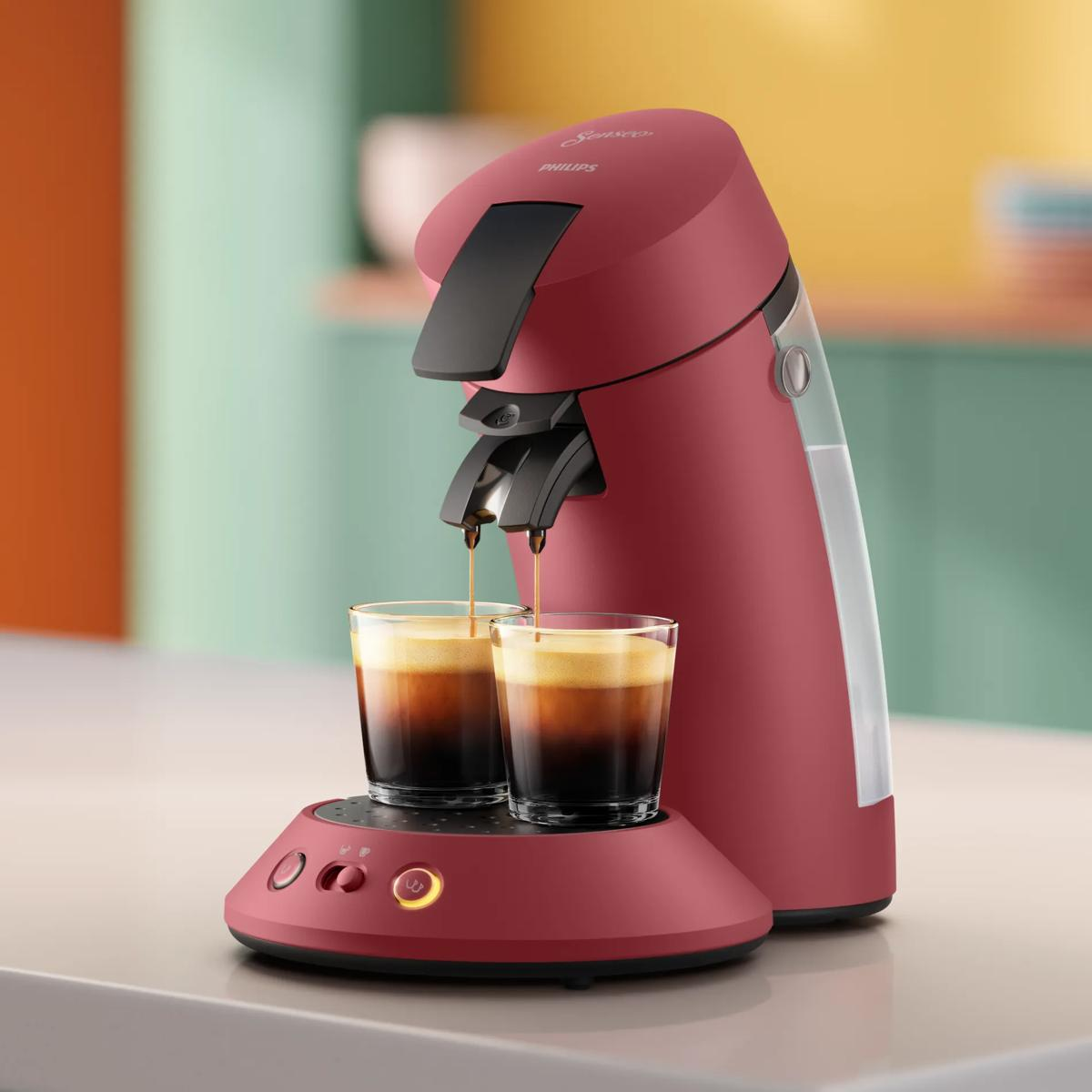 Macchina da caffè Philips rossa riempie due bicchieri con caffè su sfondo colorato.