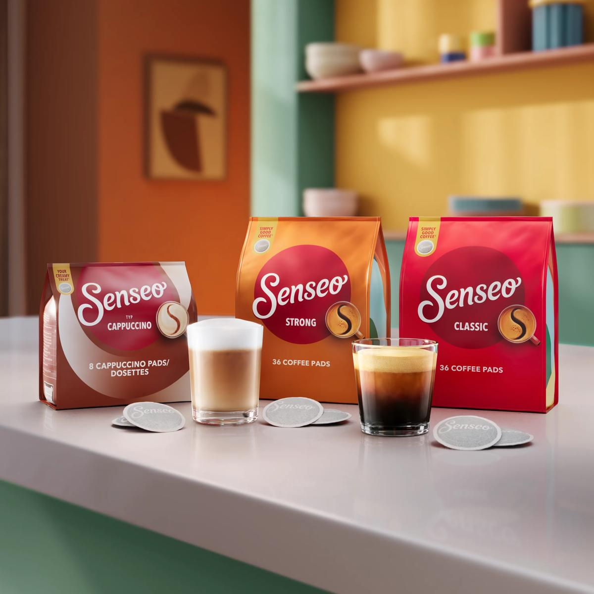 Tre confezioni di caffè Senseo, due bicchieri di caffè e cialde su un bancone in cucina.