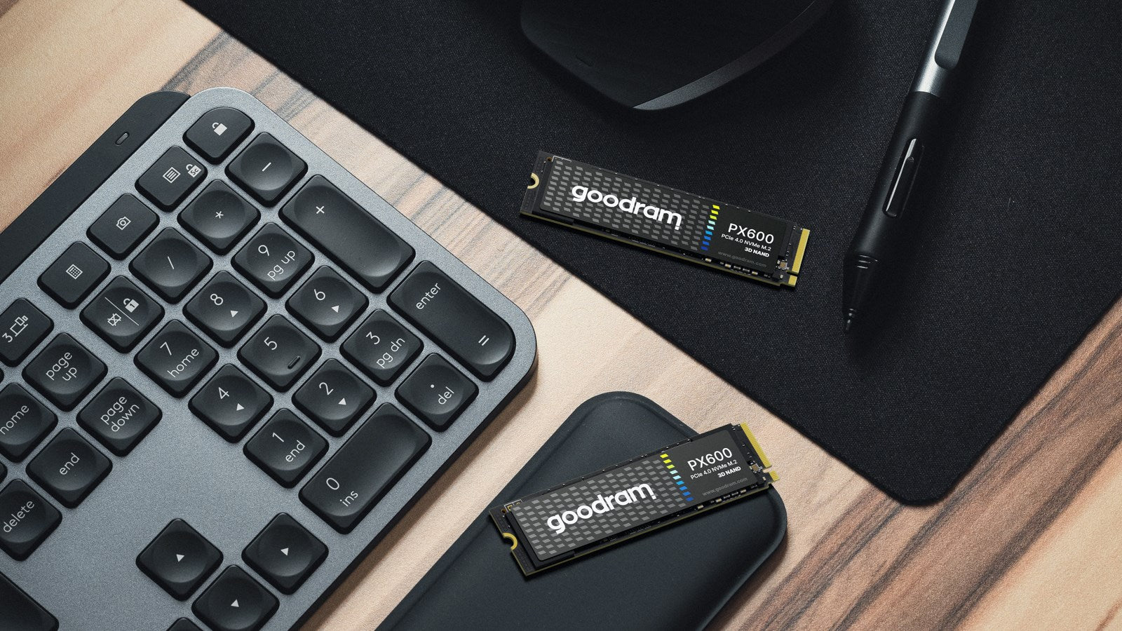 Zwei Goodram PX600 NVMe M.2 SSDs auf einem Schreibtisch mit Tastatur, Maus und Stift.
