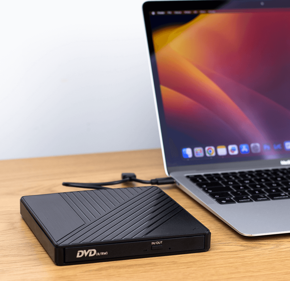 Un masterizzatore DVD esterno nero è collegato tramite cavo a un laptop argentato su una scrivania in legno.