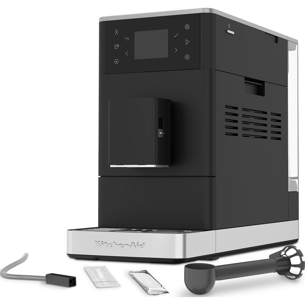 Machine à café KitchenAid noire avec accessoires comme tube à lait, poudre de nettoyage et cuillère à café sur fond blanc.