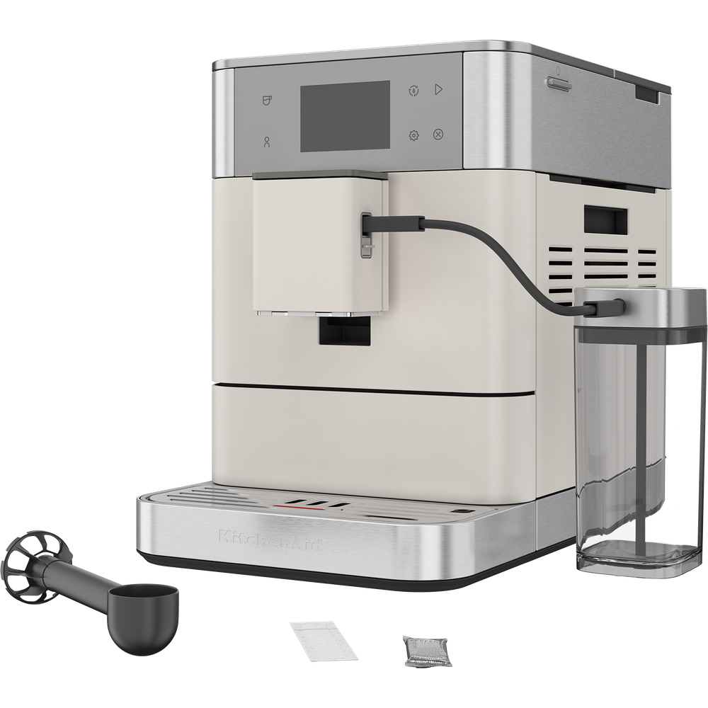 Machine à café automatique KitchenAid beige et argent avec réservoir de lait, cuillère et accessoires.