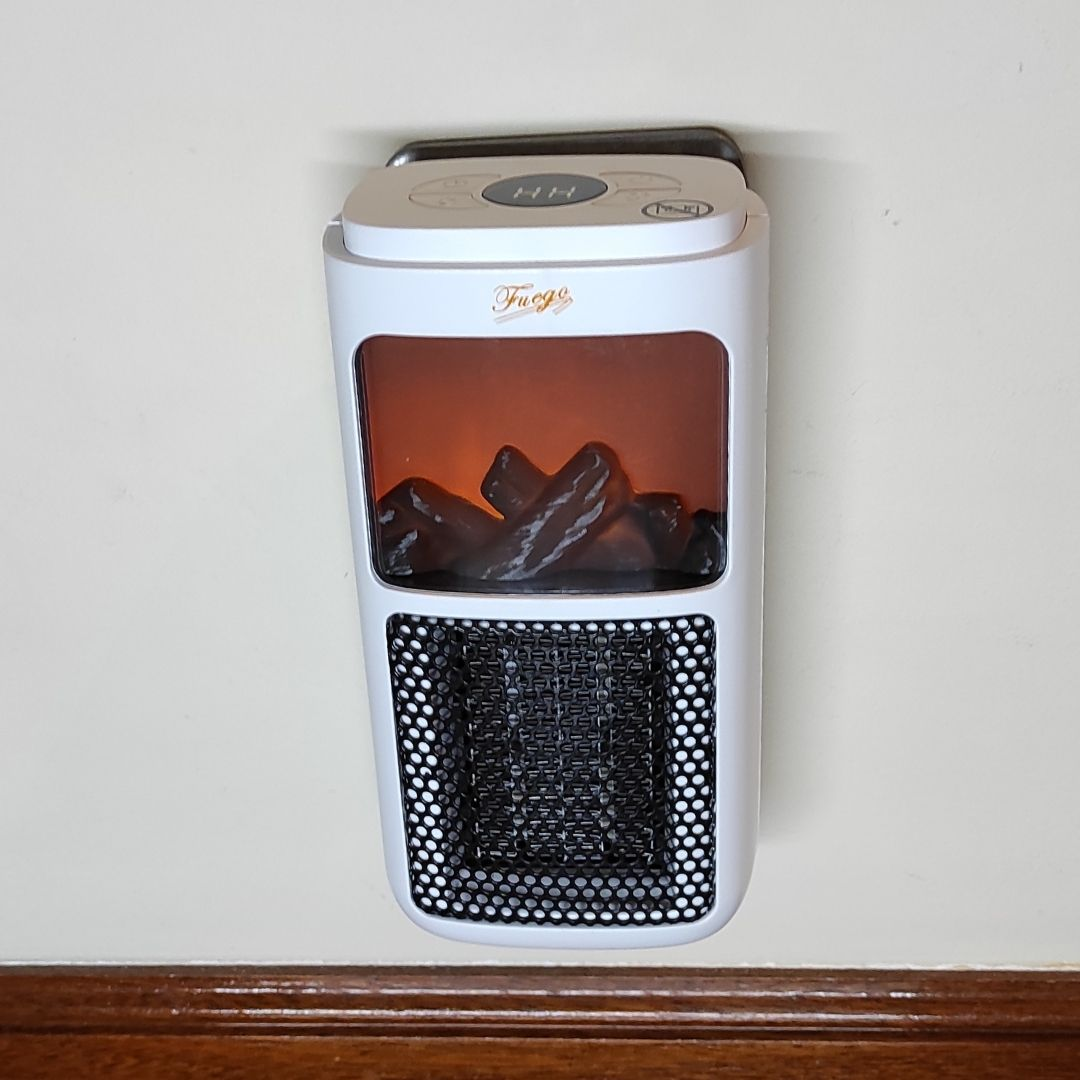 Un mini calefactor blanco con chimenea simulada y rejilla de ventilación negra en una pared.