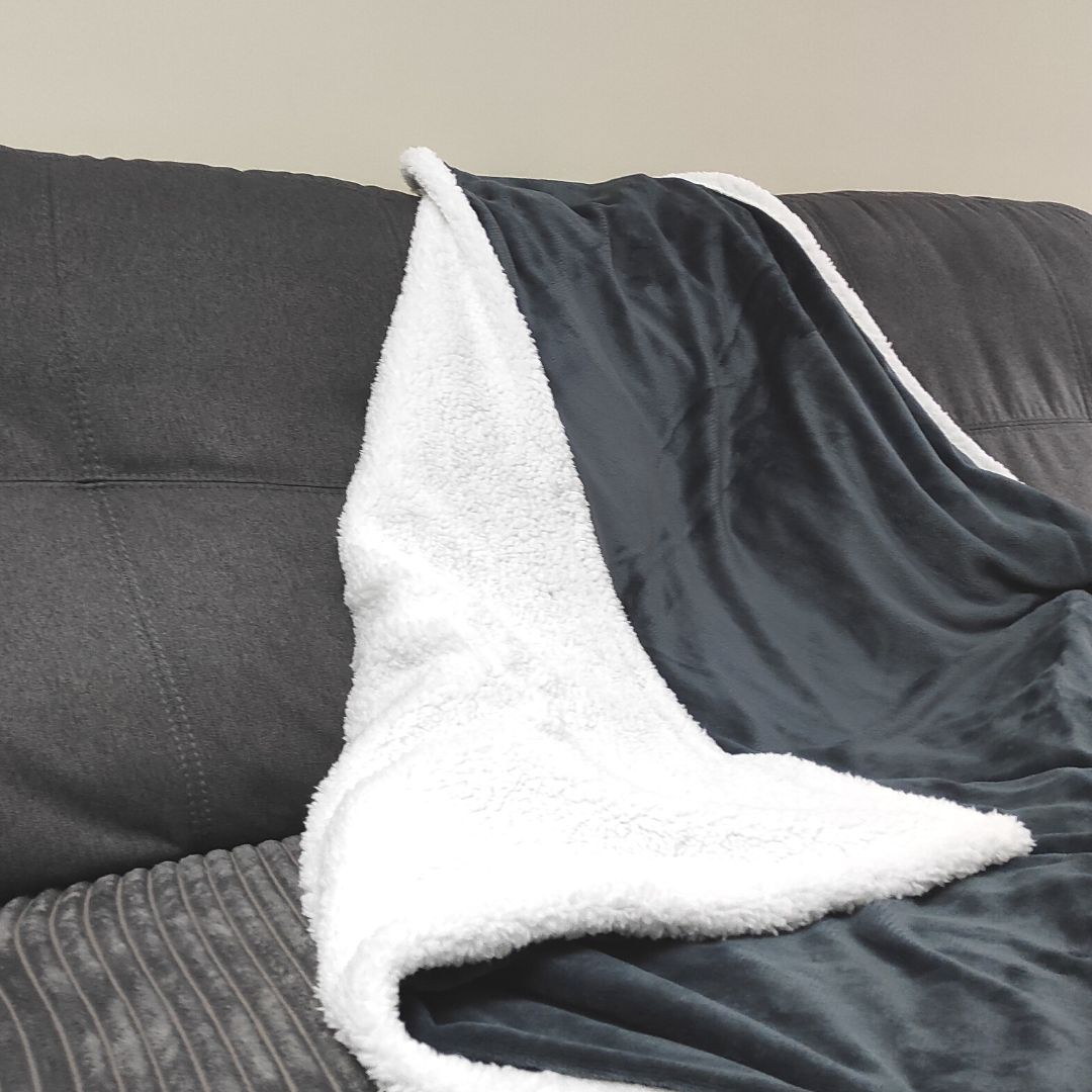 Una manta de felpa gris oscura y blanca sobre un sofá oscuro ante una pared.