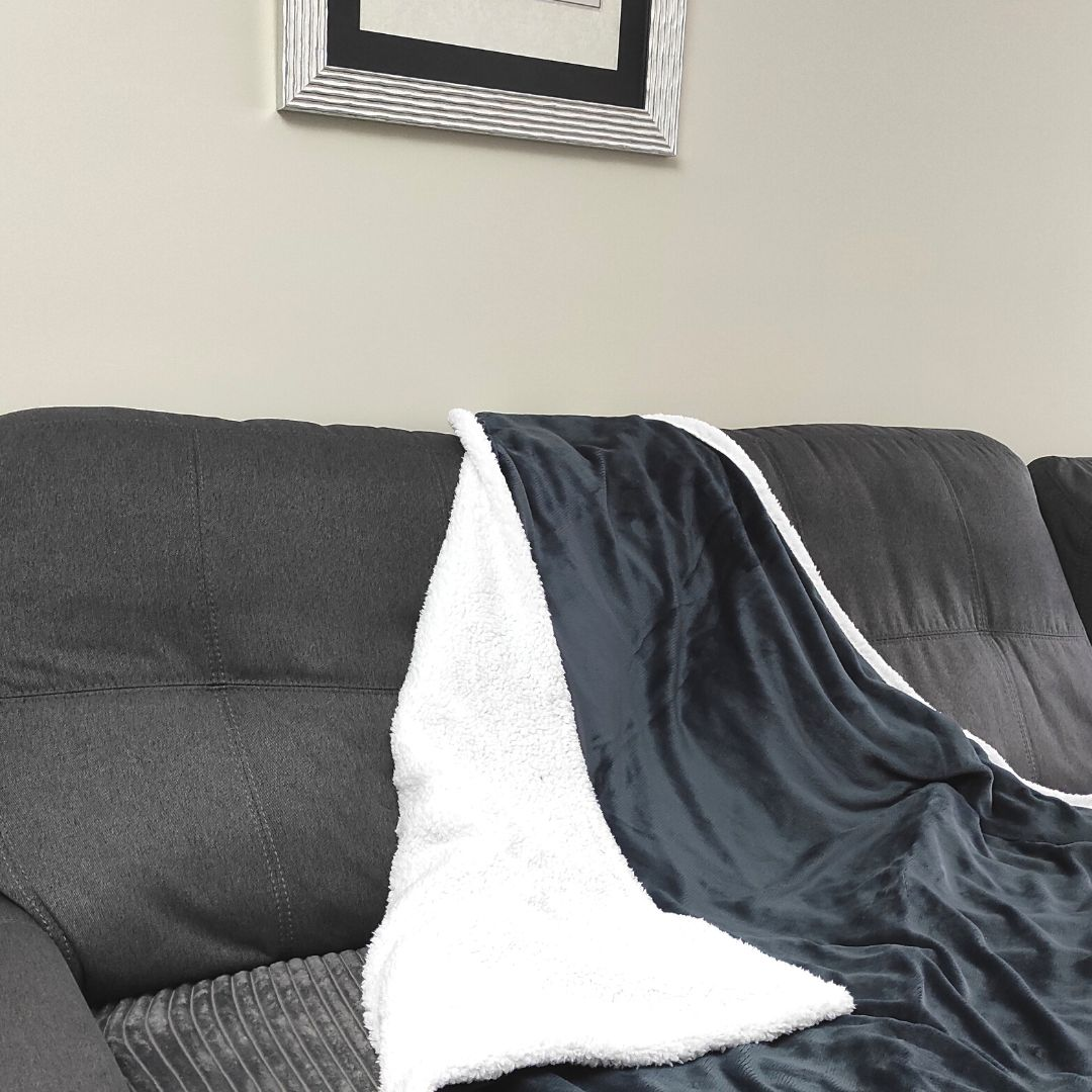 Una manta de sherpa gris y blanca sobre un sofá oscuro, con un cuadro en la pared.