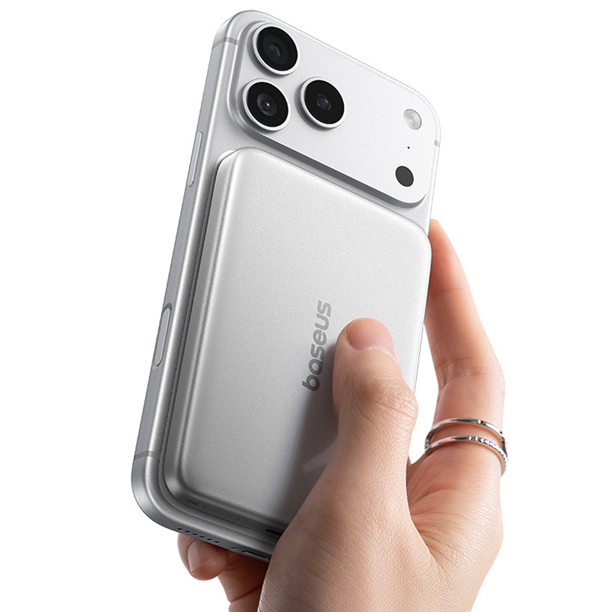 Una mano sostiene un smartphone plateado con una batería externa magnética Baseus en la parte trasera.