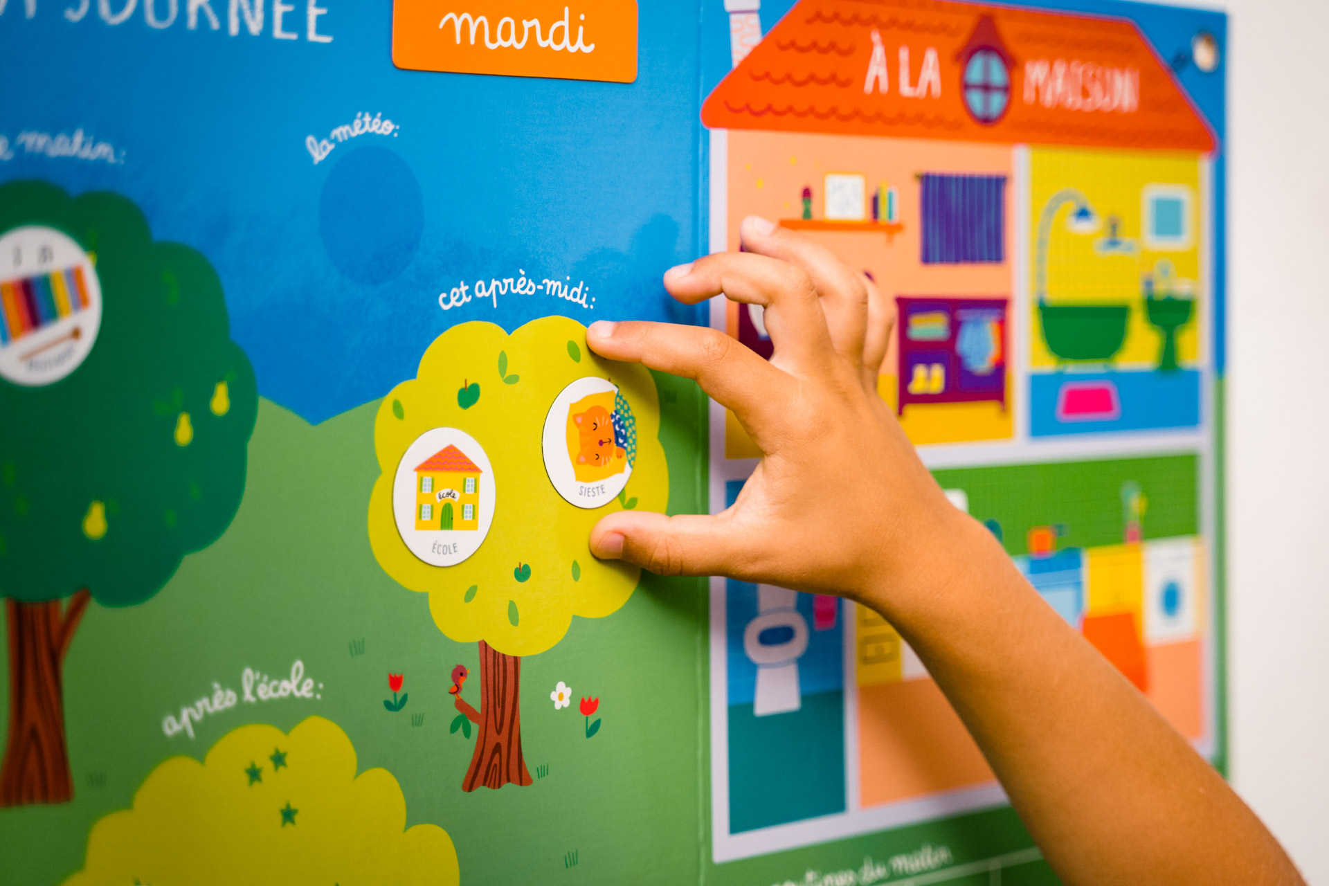 Ein Kindertischkalender zeigt eine bunte Spielszene mit Häusern, Bäumen und Symbolen.