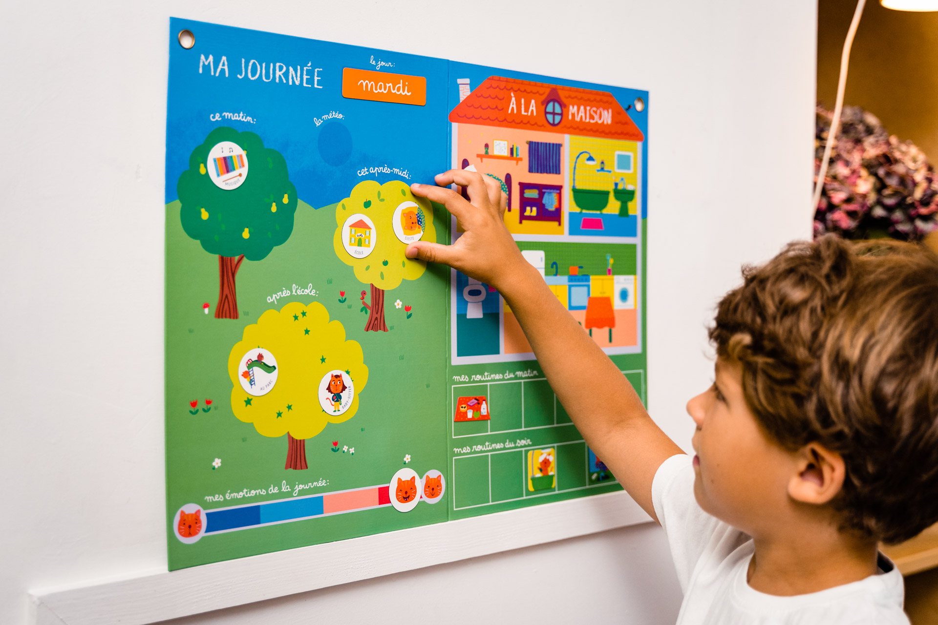 Ein junger Junge interagiert mit einem bunten Tagesablauf-Diagramm an einer weißen Wand.