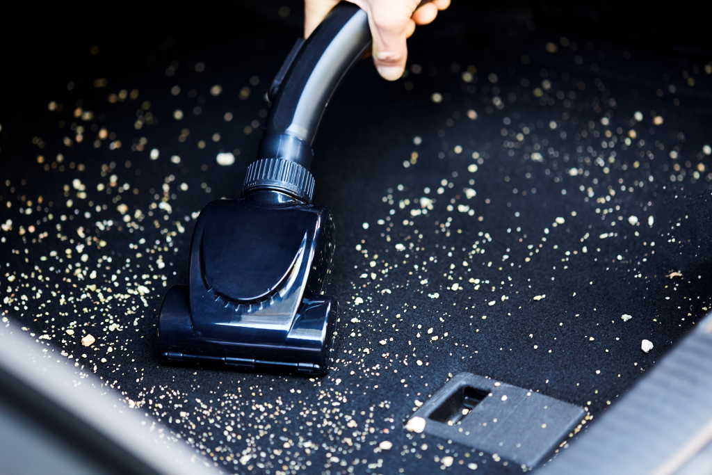 Un aspirateur nettoie le tapis de coffre d'une voiture couvert de miettes.
